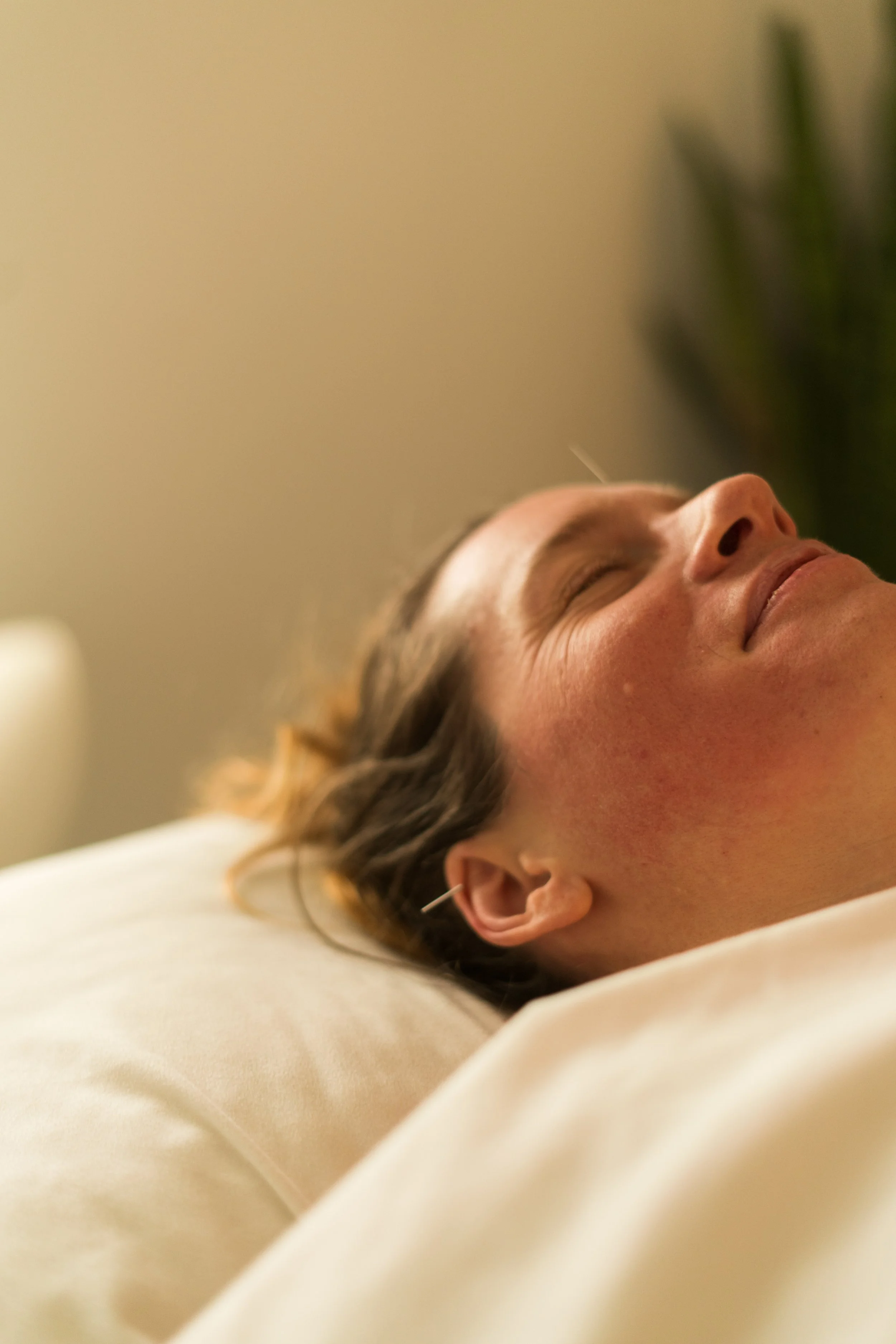 A woman is lying down with her eyes closed, appearing to be resting or asleep, in a peaceful setting.