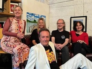 Group of five people, three women and two men, gathered in an art gallery or studio with framed artwork on the walls, smiling and posing for the photo.