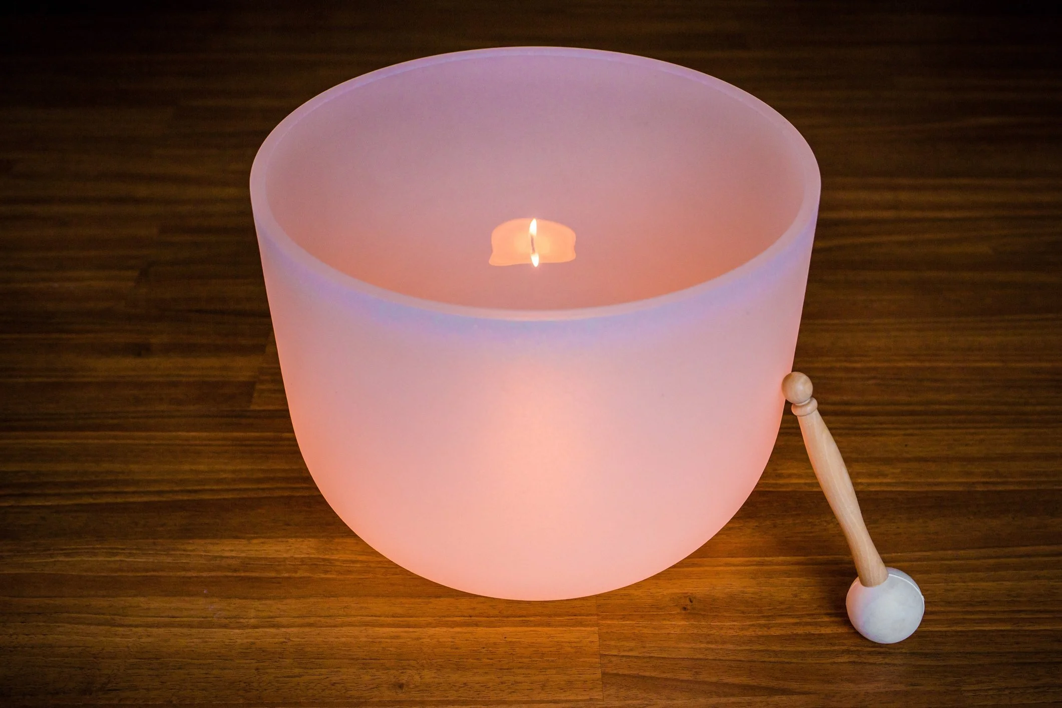 A pink flameless candle with a faux flame on a wood surface, with a small wooden ball and a small white ball on the side.