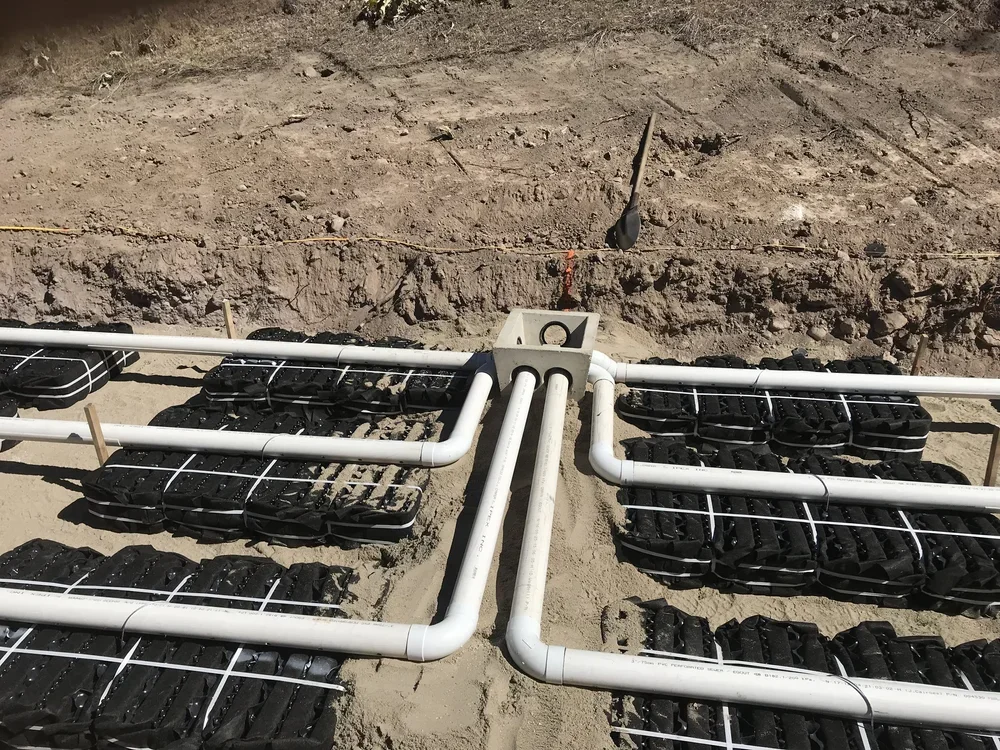 White distribution pipes connected to septic field chambers during installation.
