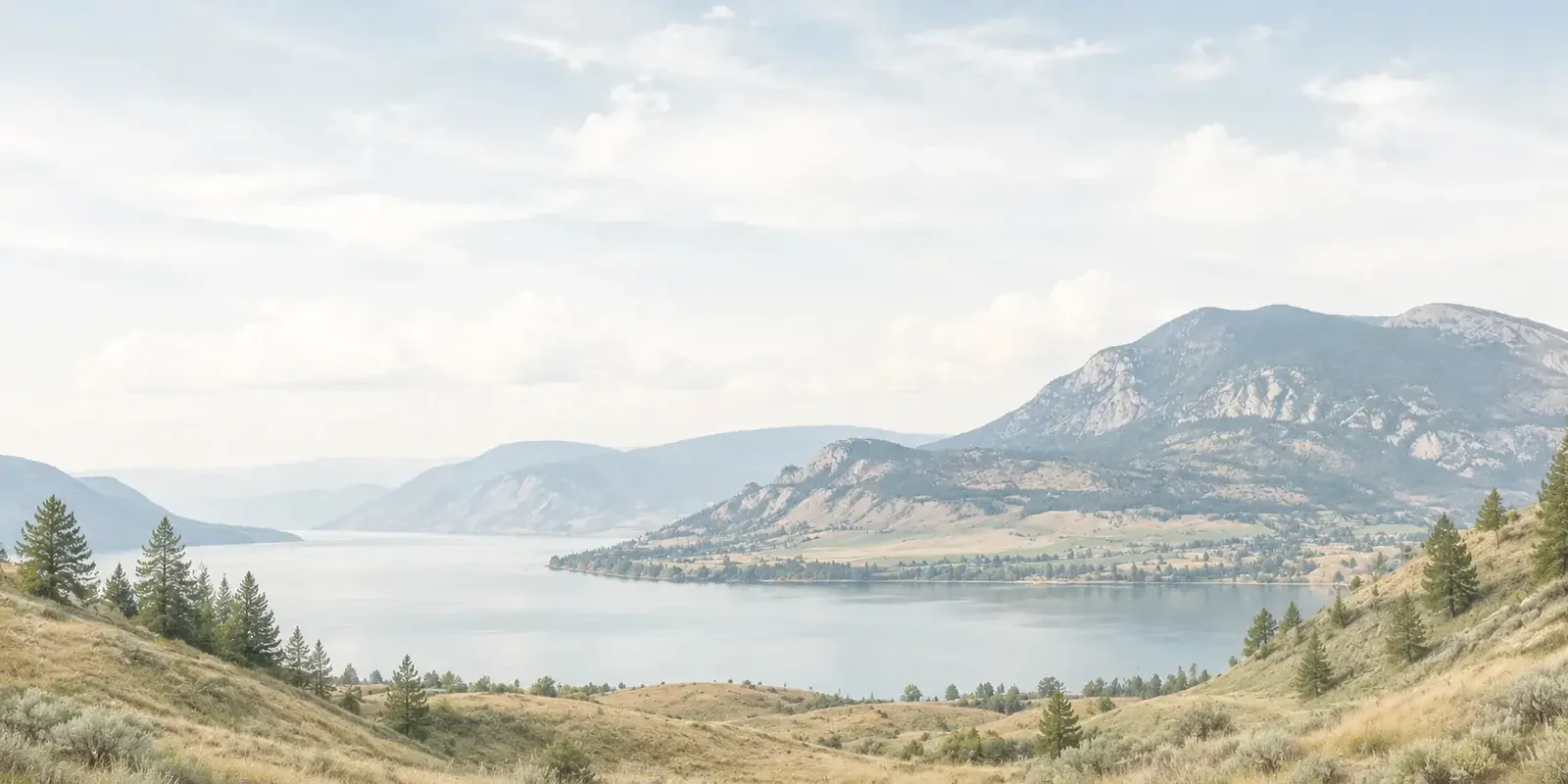 Scenic lake surrounded by mountains, dry grassland hills, and pine trees in the South Okanagan, British Columbia.