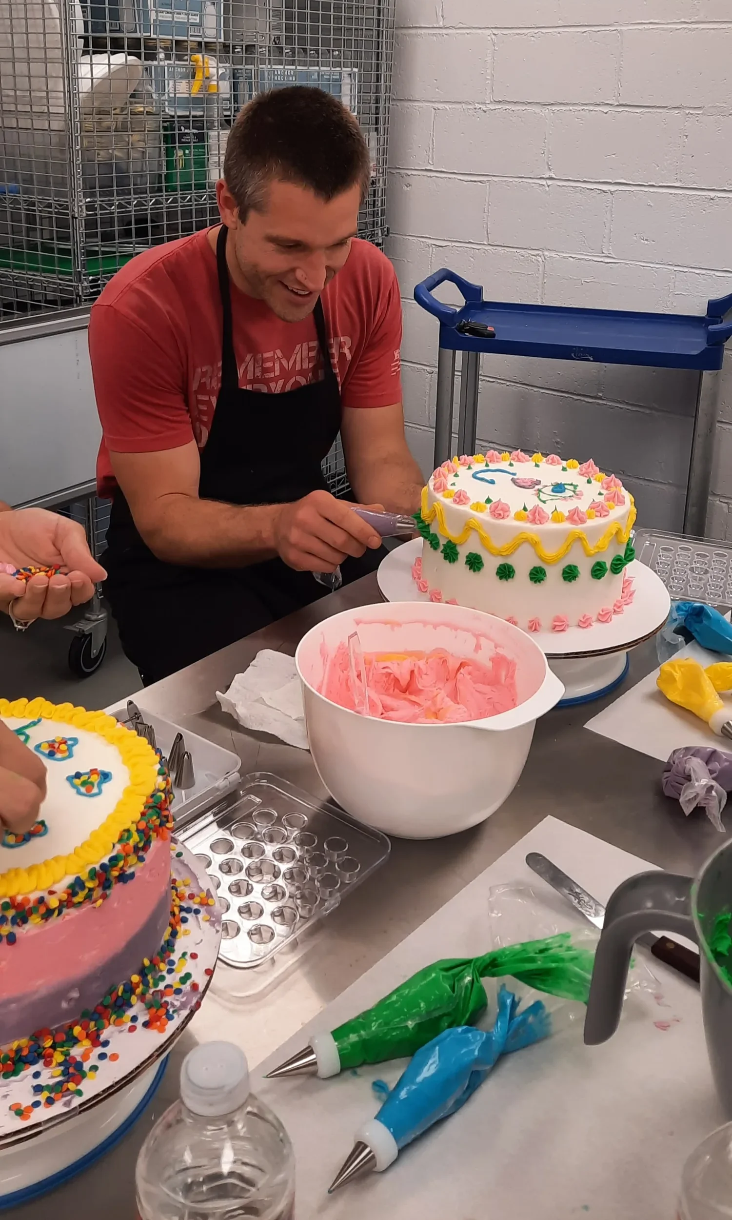 A man smiling piping buttercream onto his finished layer cake during a cake decorating class