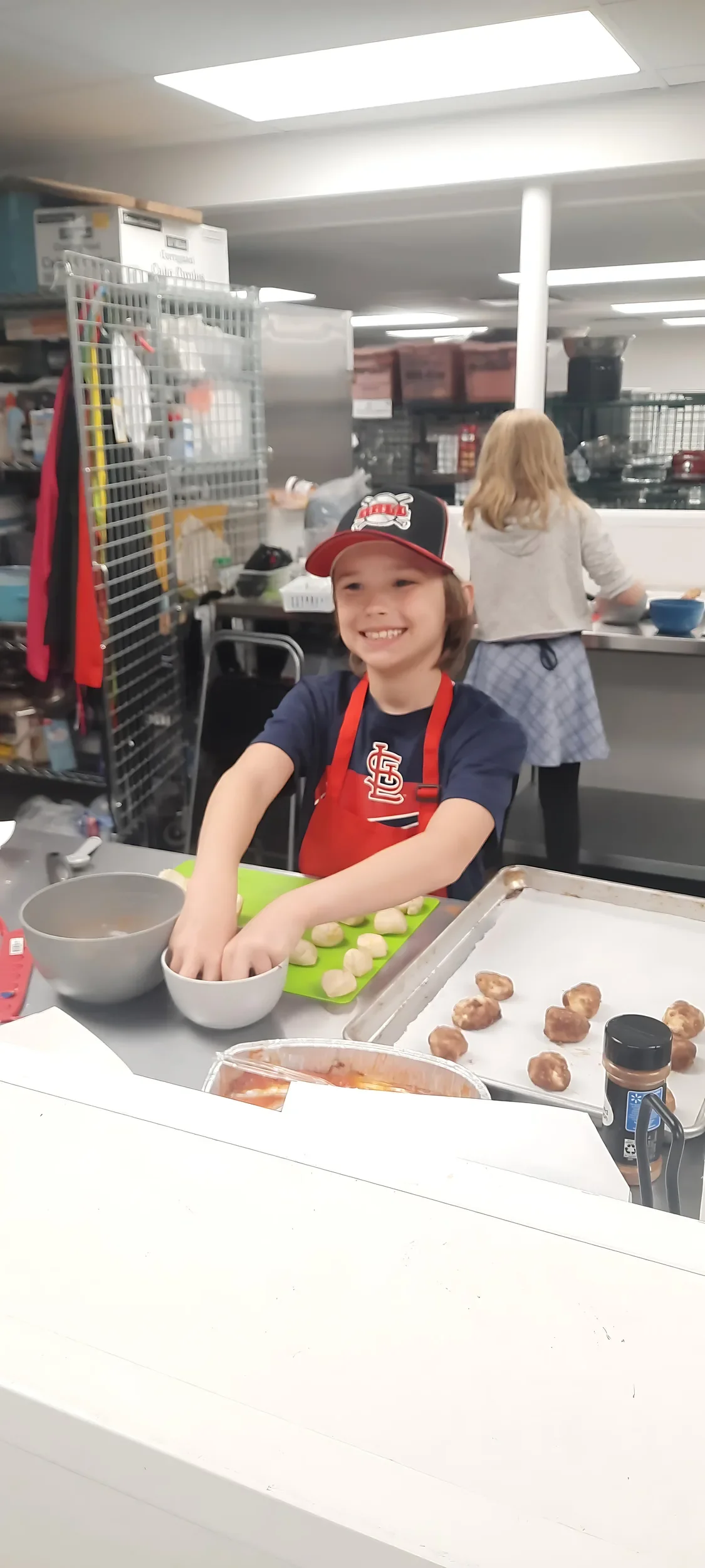 Young boy in apron smiling while he rolls his donuts in cinnamon and sugar during the kids culinary cooking club class.