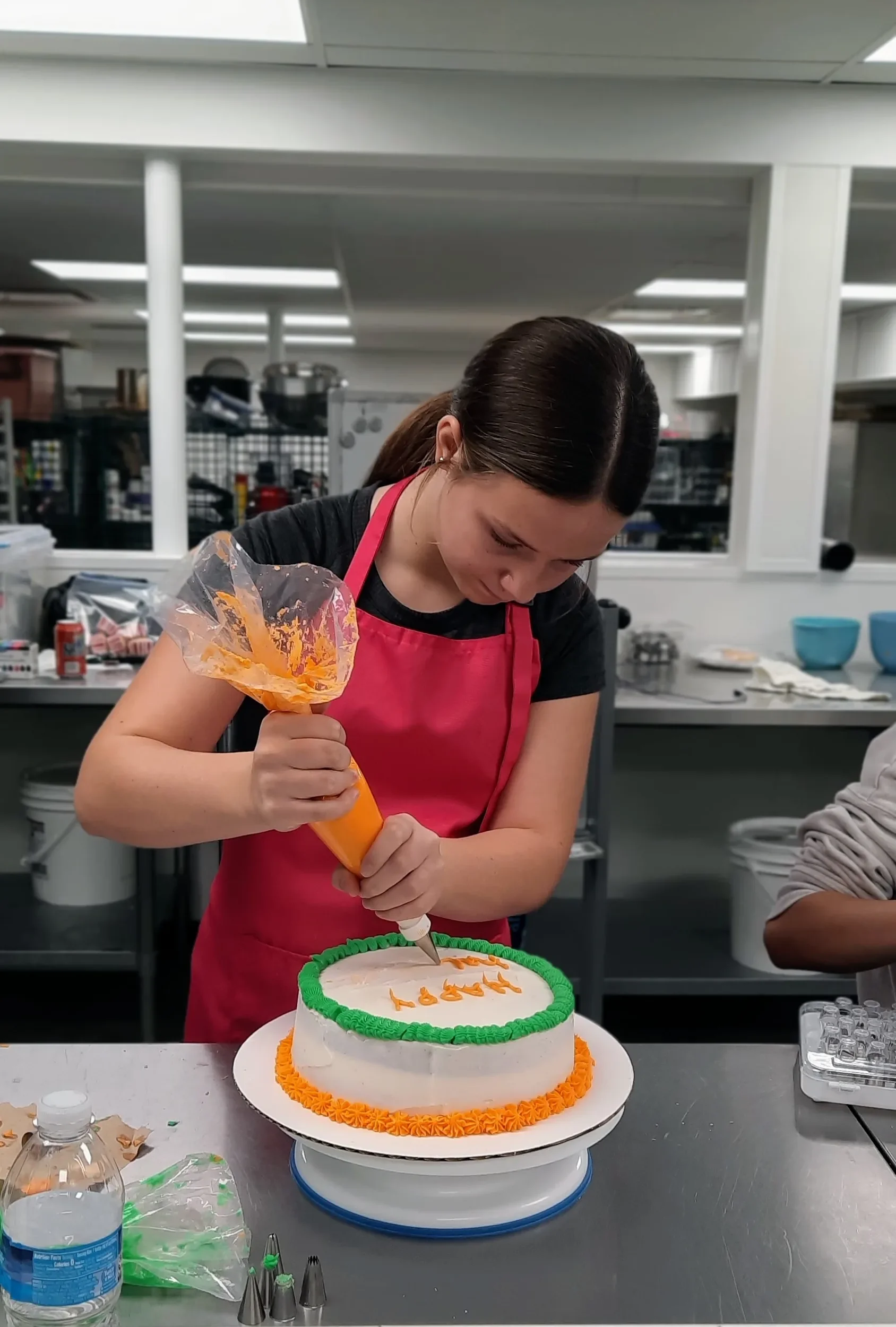 A teen piping on her finishing touches to her layered cake during a cake decorating class