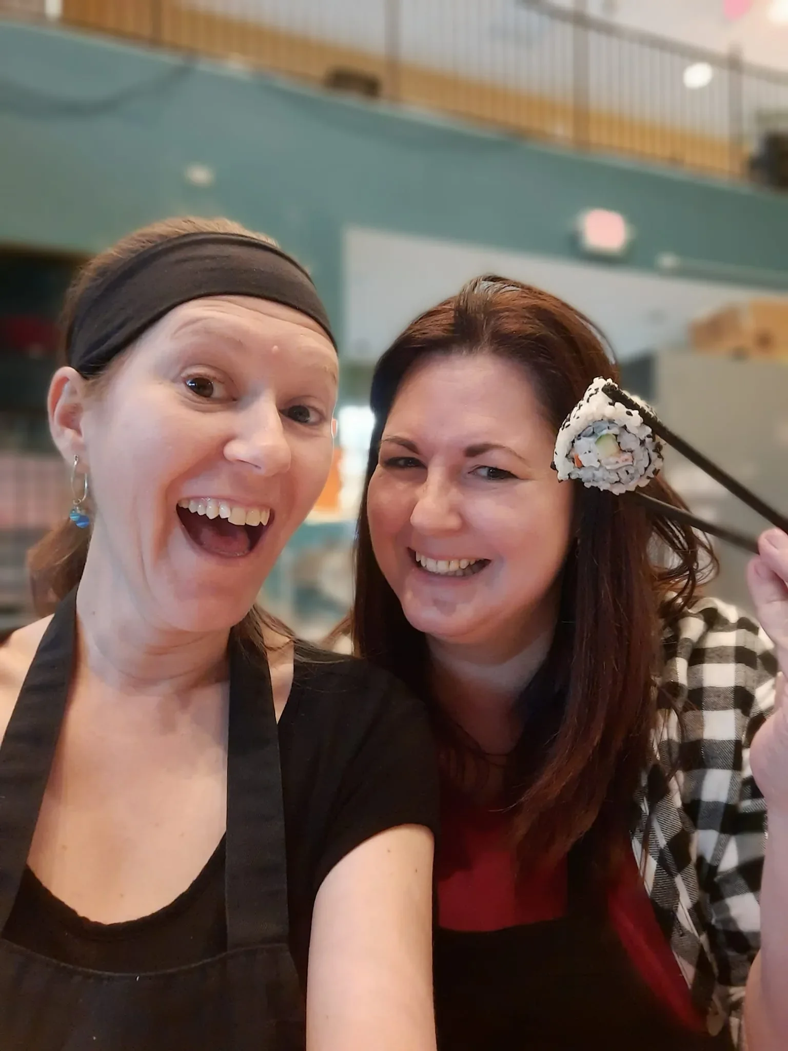Friends smiling and laughing while one holds up her sushi with her chopsticks during a sushi class