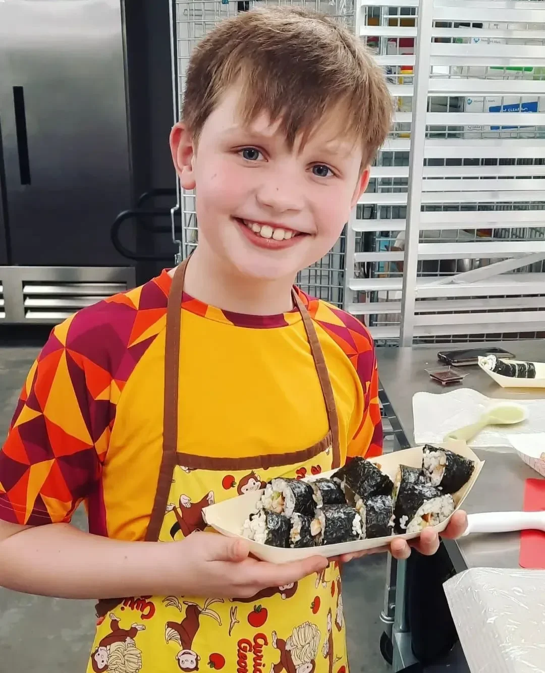 Child holding up his plated sushi with a smile during a sushi class