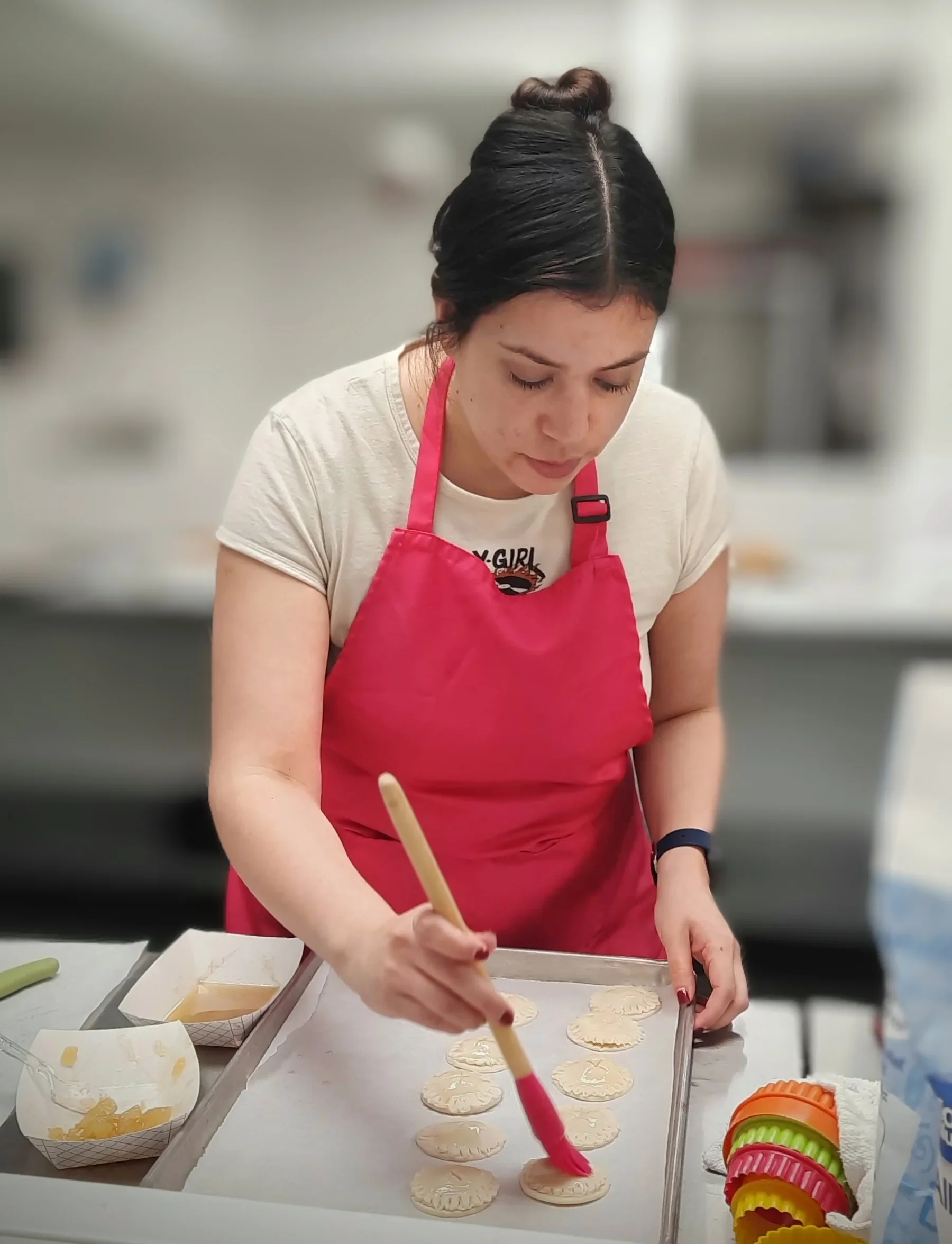 Adult student with a pink apron brushing butter onto her apple pie cookies with a pastry brush