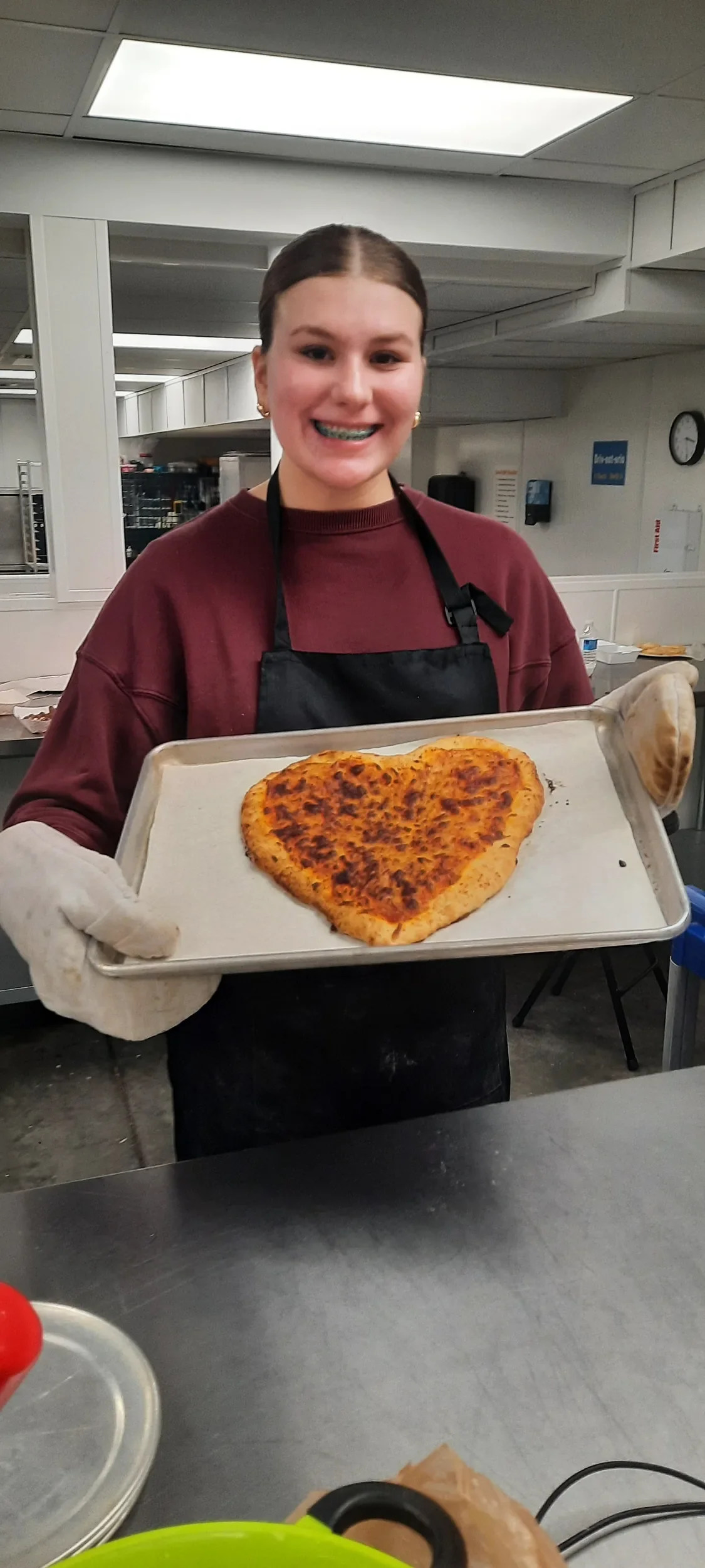 A teen holding her heart shaped pizza she made during cooking class.