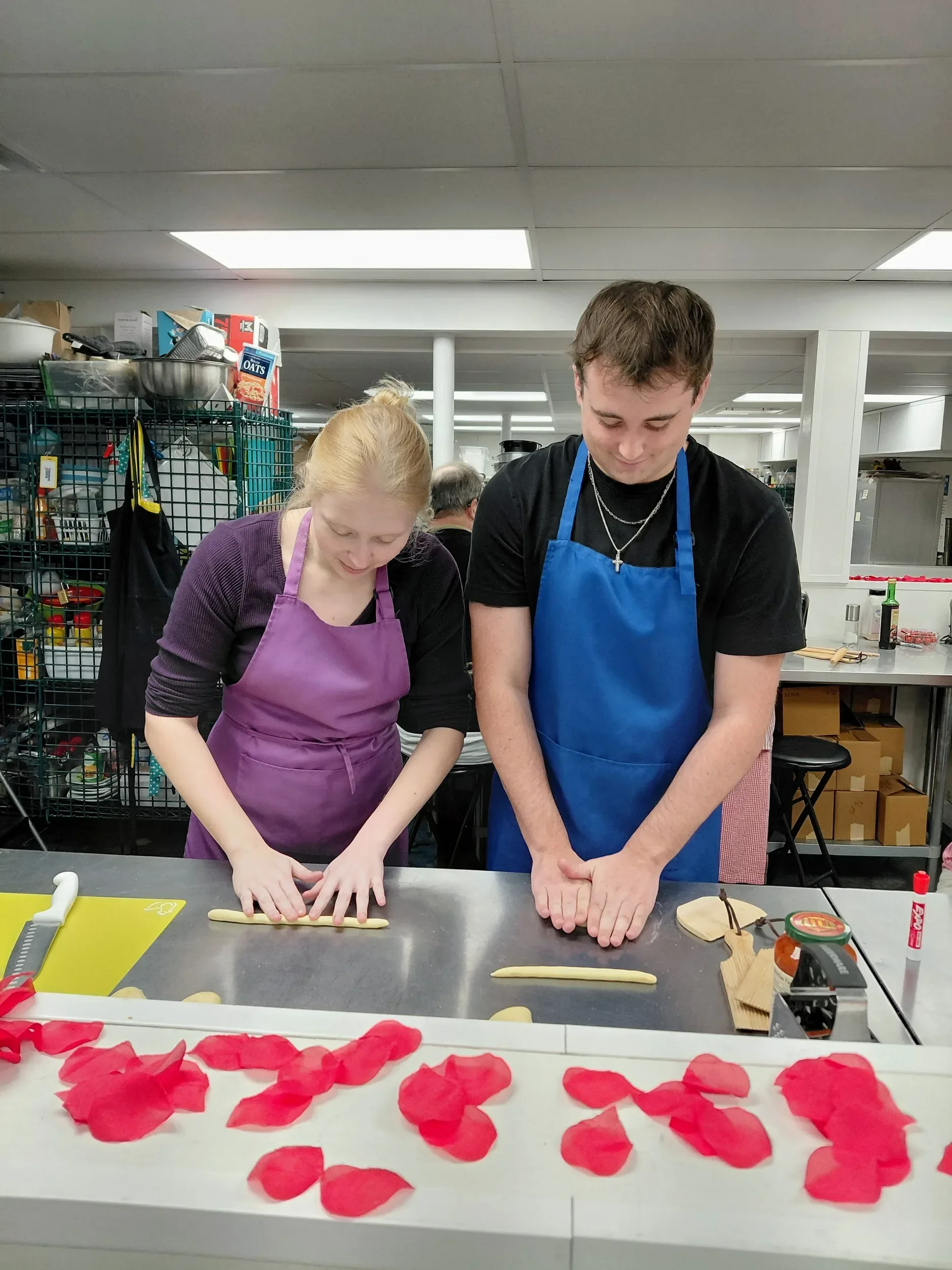 Couple, one with a purple and one a blue apron,  rolling out dough before hand cutting their cavetelli noodles during a cooking date night class