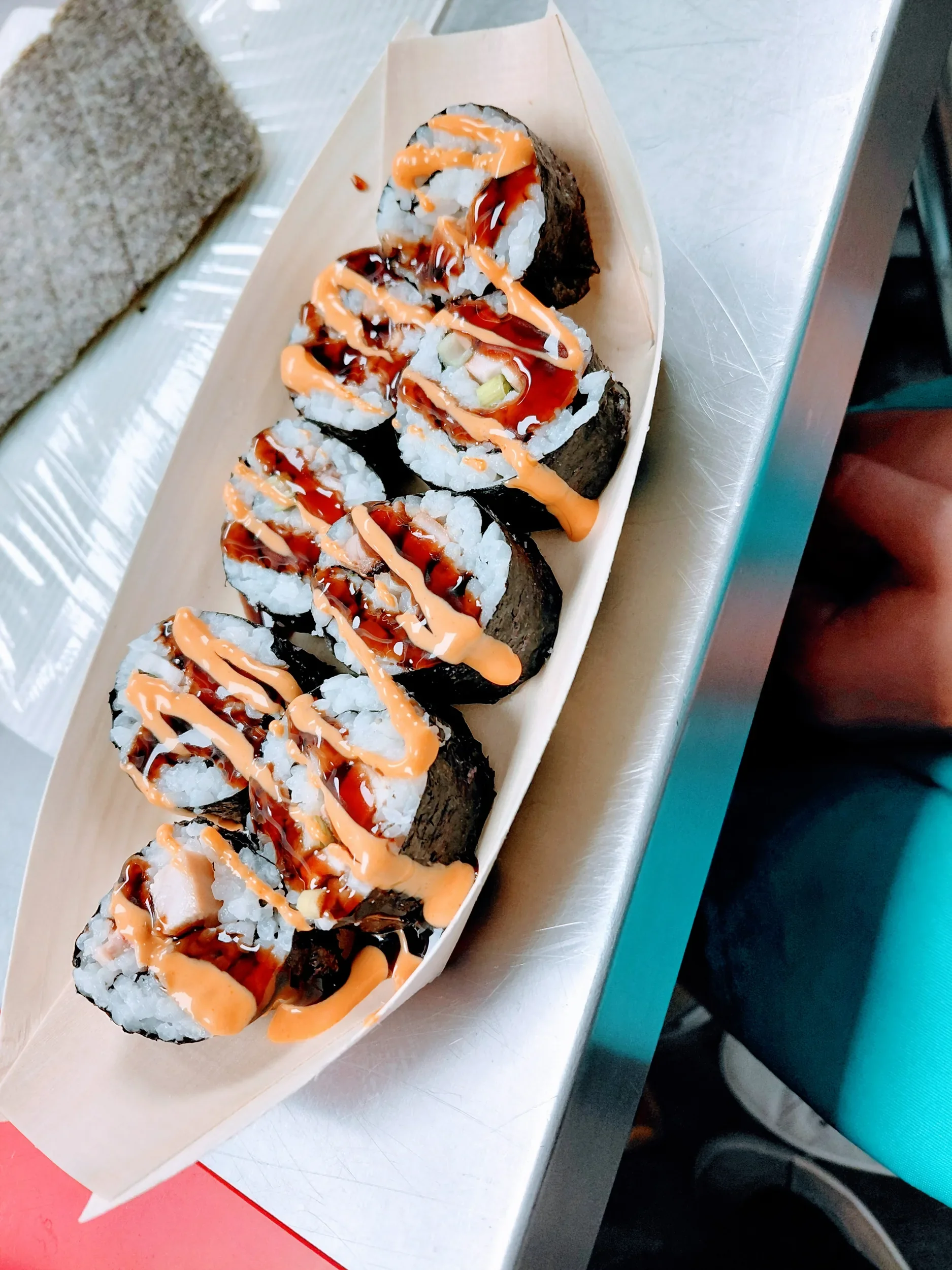 Sliced sushi rolls in wooden boat drizzled with spicy mayo and eel sauce