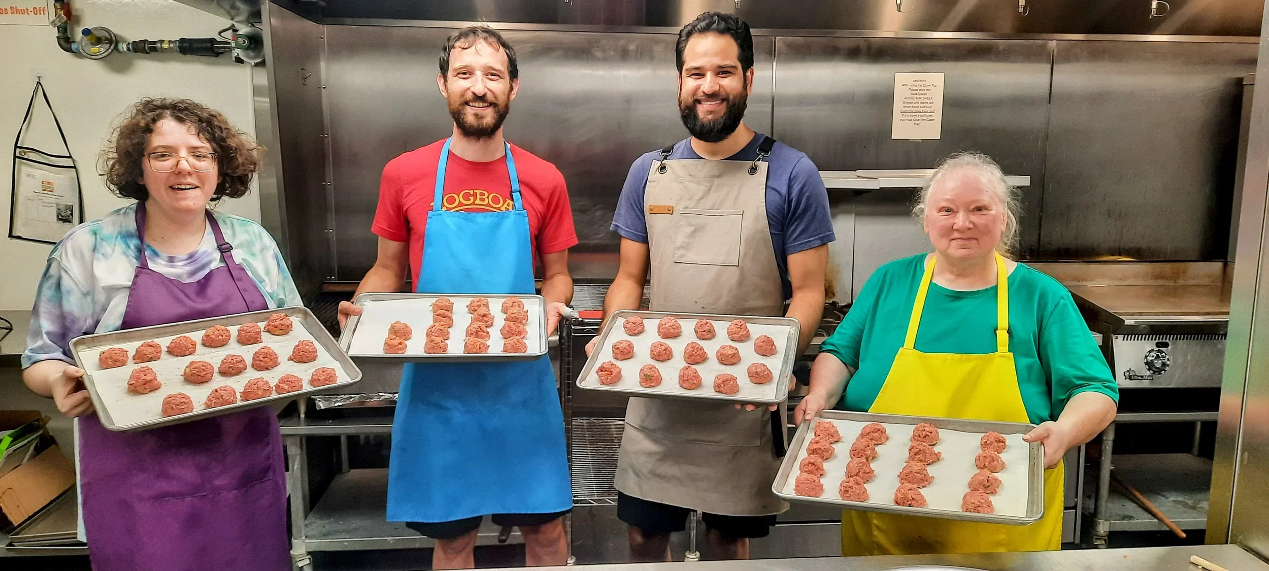 Adult students with their aprons on holding a sheet pan with meatballs ready to back all smiling