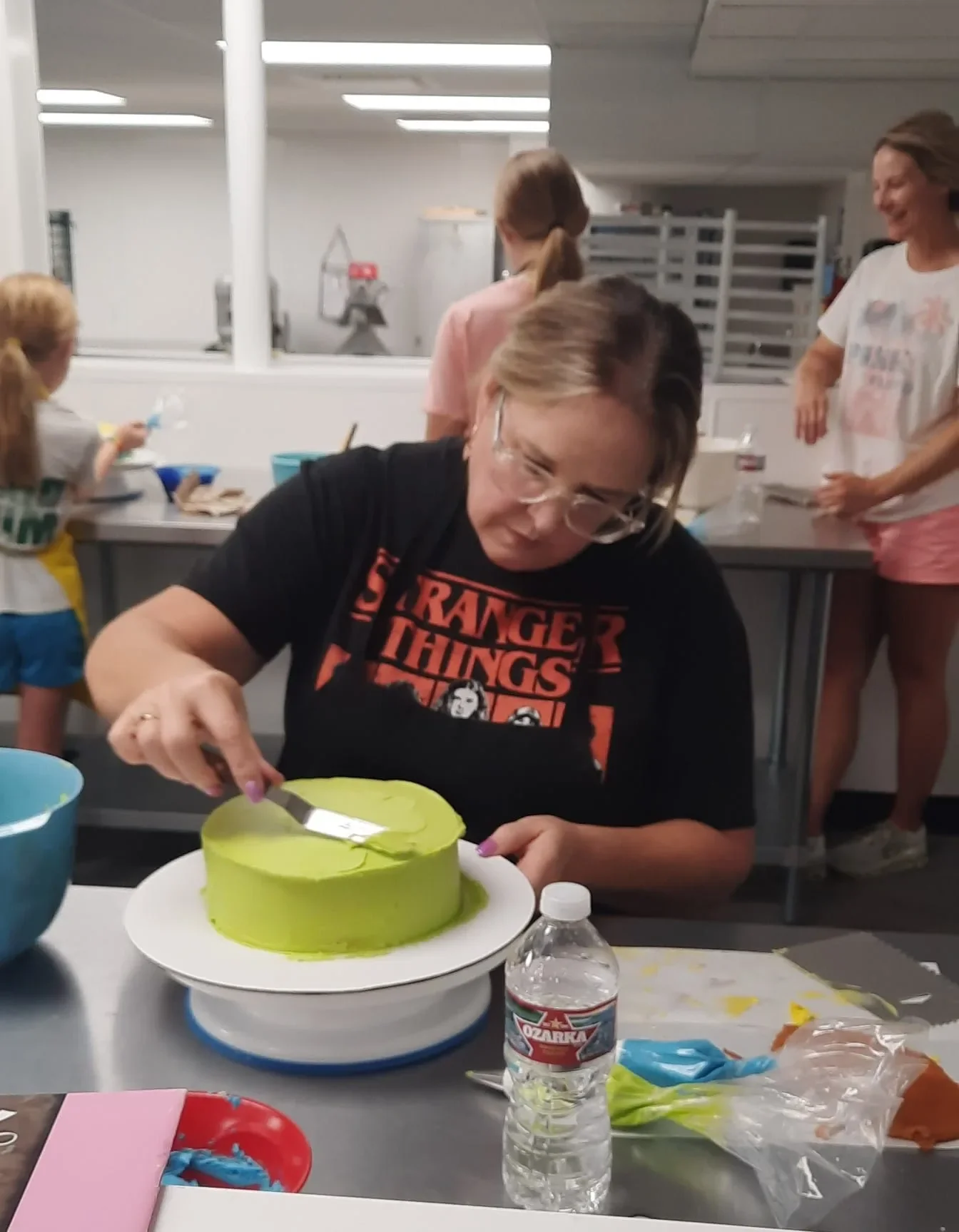 Adult smoothing green buttercream onto a round cake during a cake decorating class