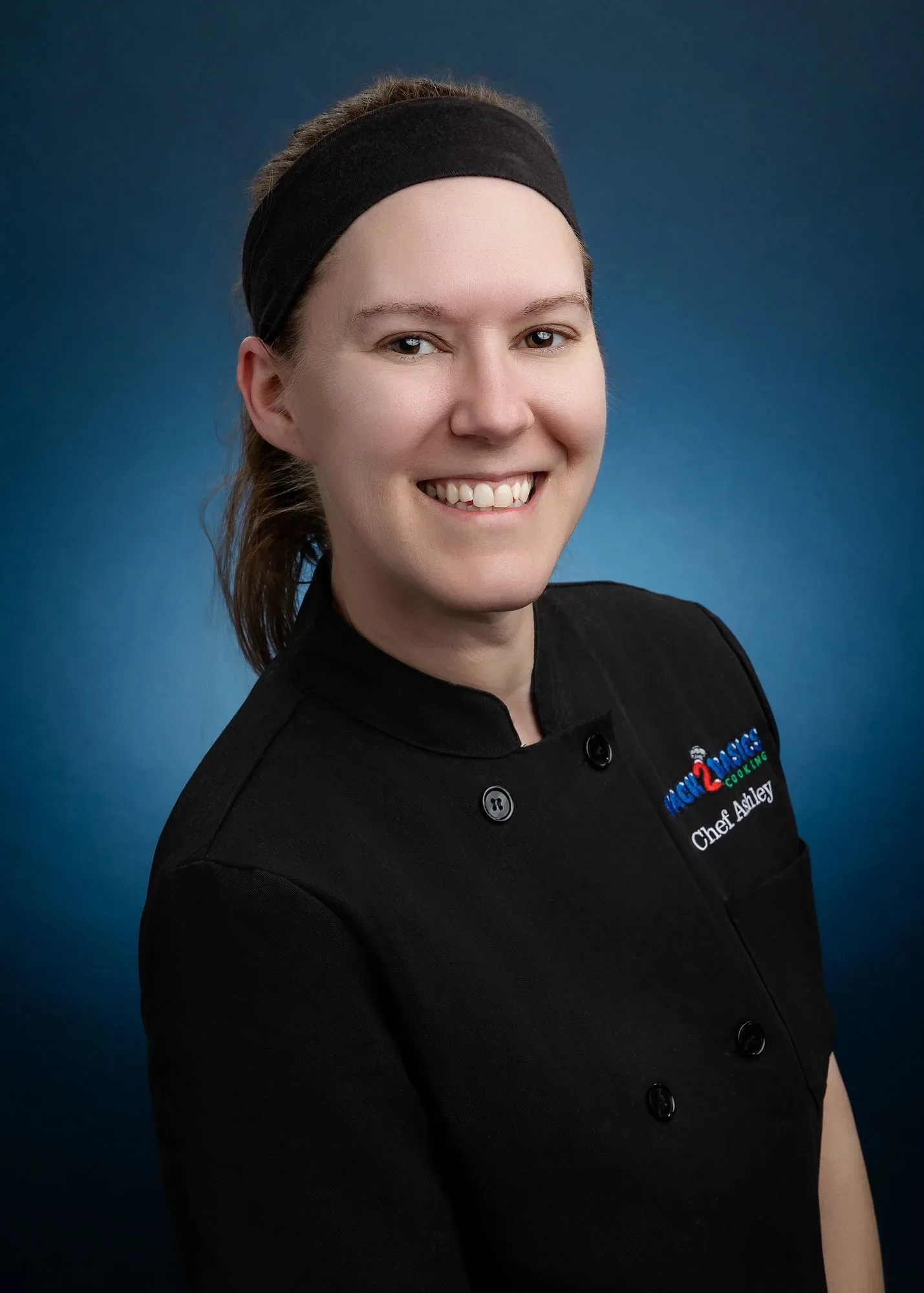 Chef Ashley smiling in a black chef coat, founder of Back 2 Basics Cooking in Columbia, MO