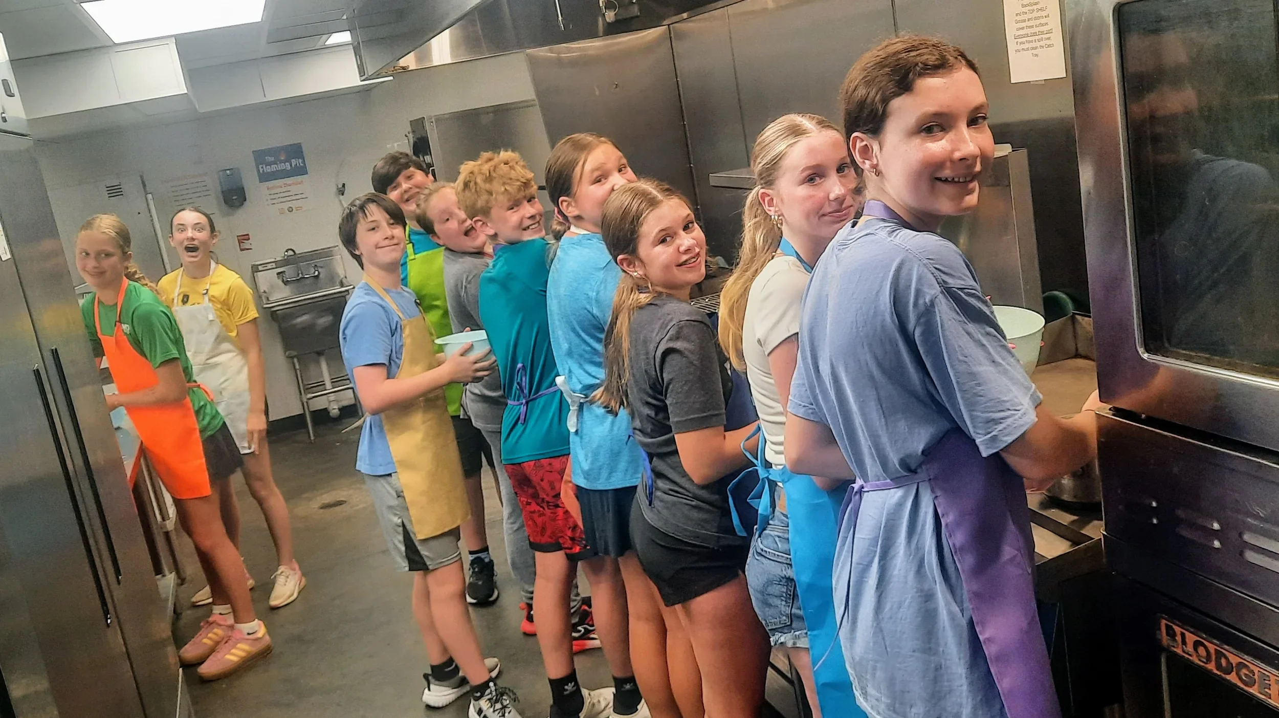 Teens standing in a line at a the Stove cooking during cooking camp with smiles