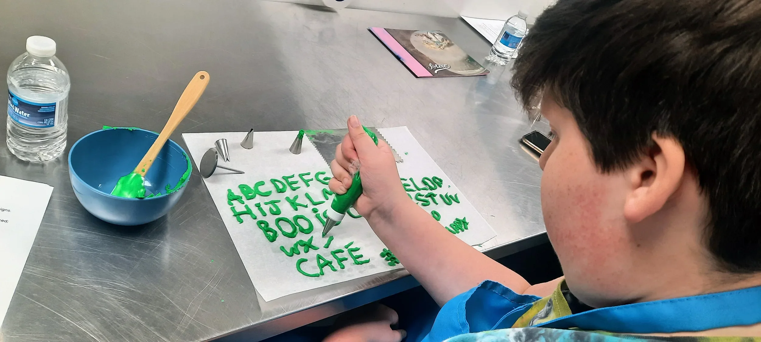 A teen practicing his piping skills with green buttercream icing during a class