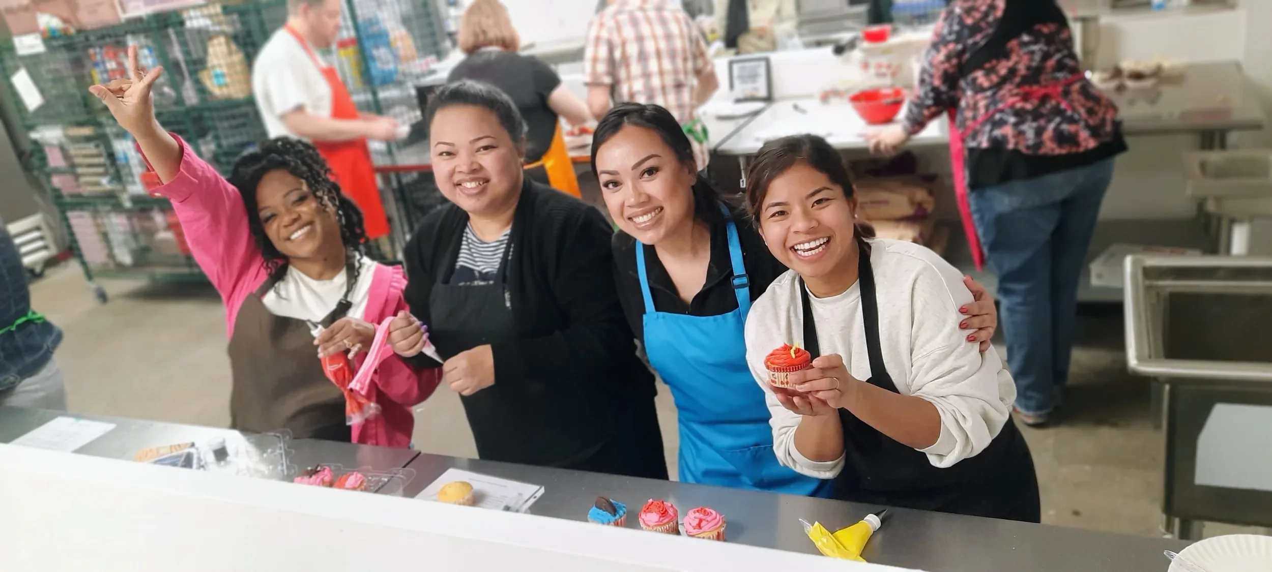 Four friends smiling holding up their cupcakes or a piping bag with icing