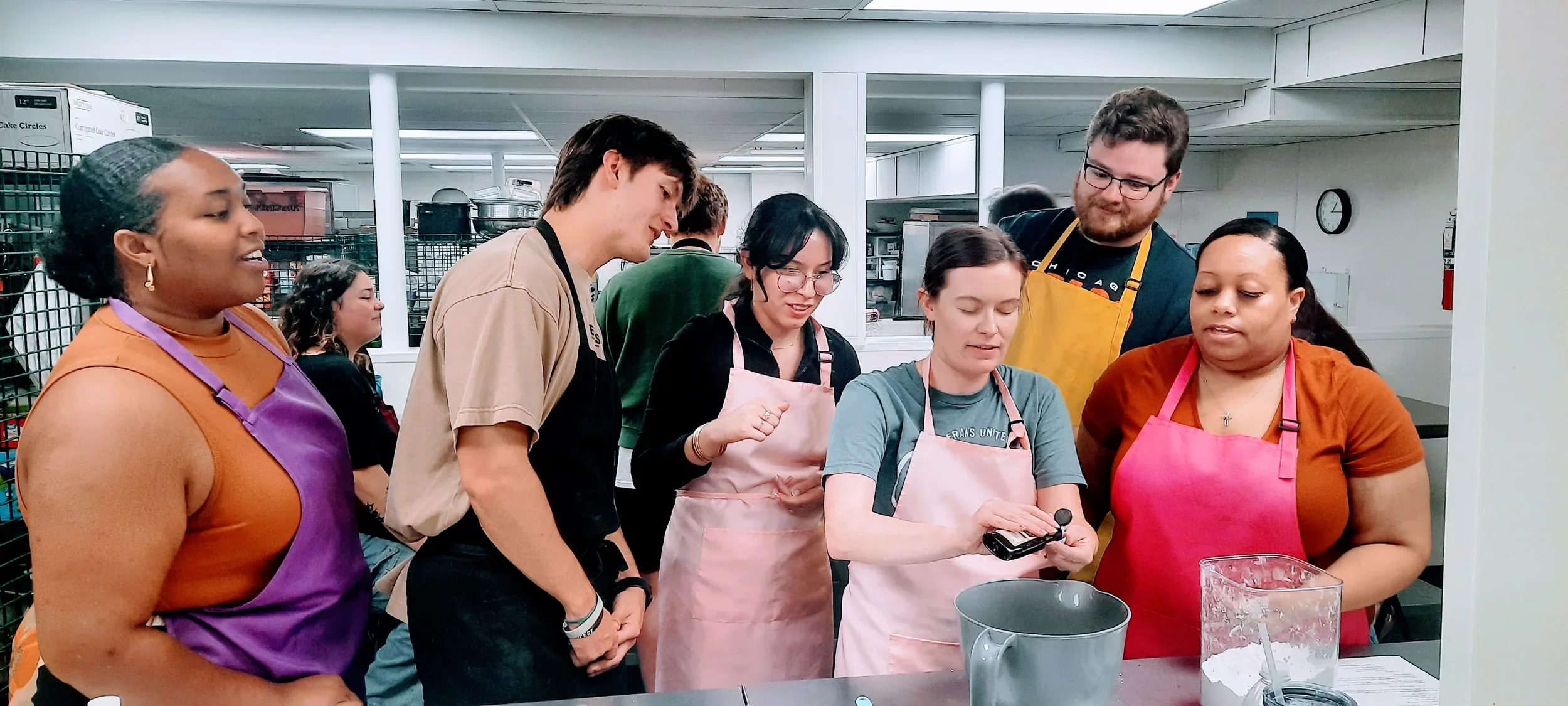 Team members from Veterans United watching their coworker measure the vanilla to tell her when to stop during a team-building cooking class in Columbia, MO.