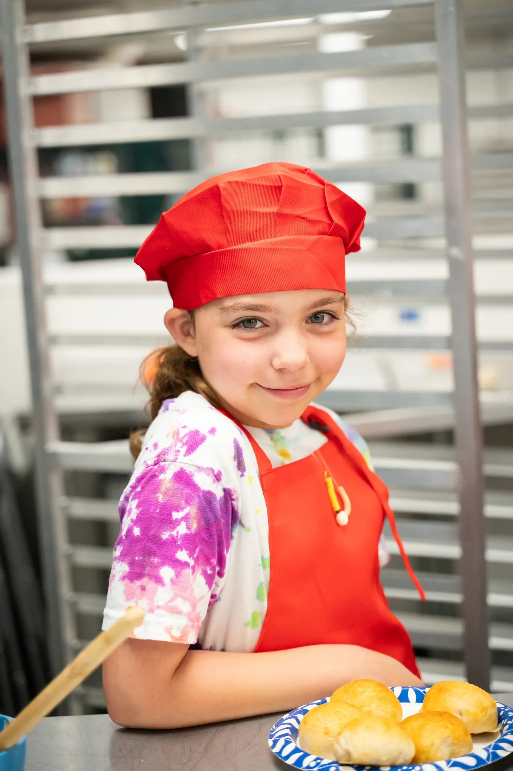Young chef in red apron and chef hat smiling standing behind her cheesy ranch chicken bombs that she prepared during cooking class