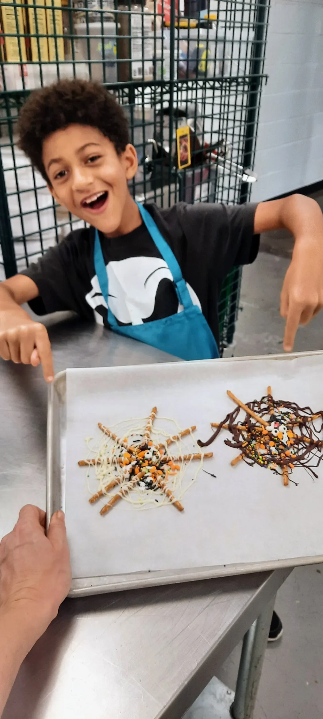 A boy smiling while pointing at the chocolate spiderweb pretzels he just made in the kids culinary cooking club class.