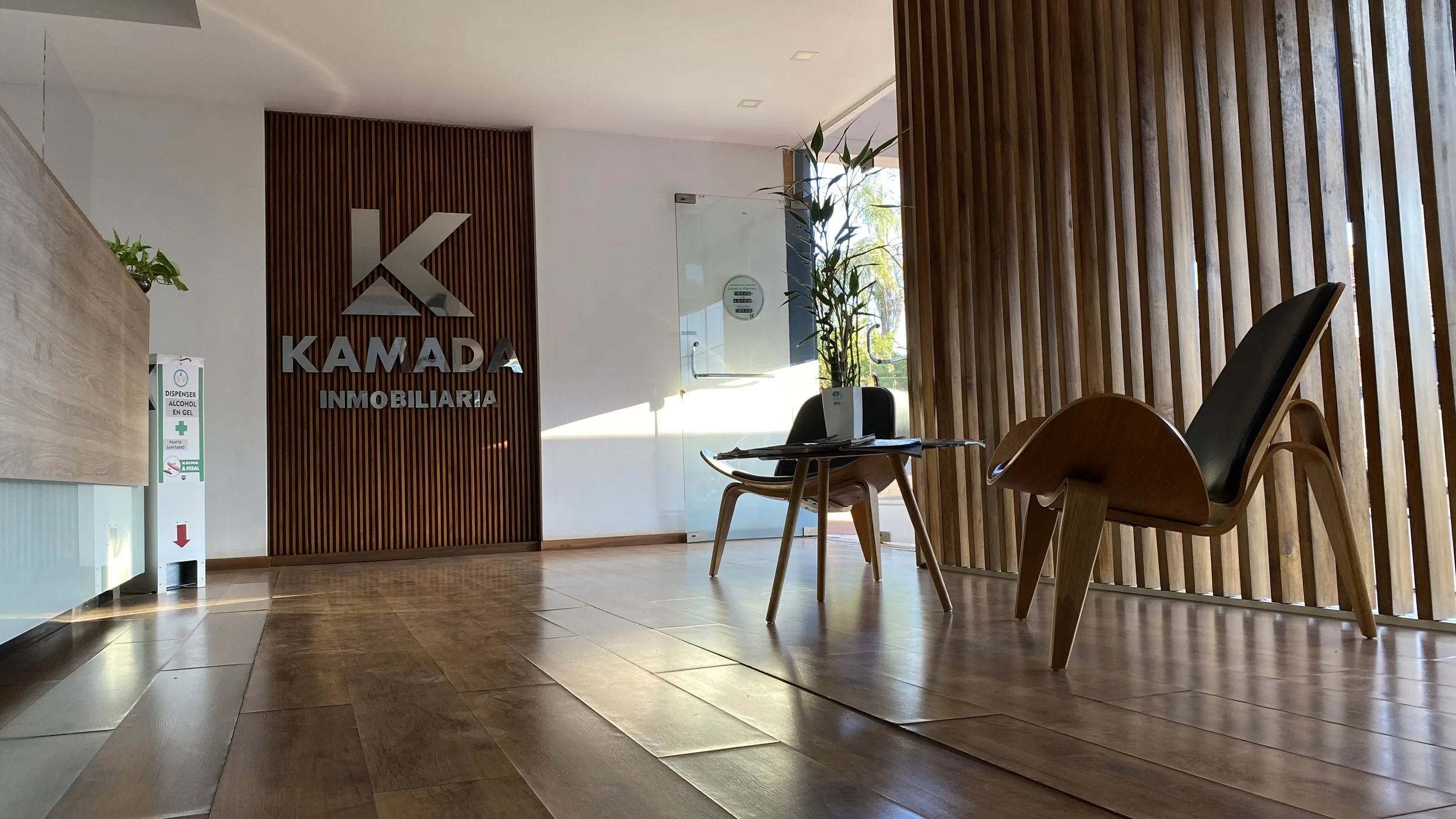 Recepción de una inmobiliaria con logo y mobiliario de madera y plantas decorativas.