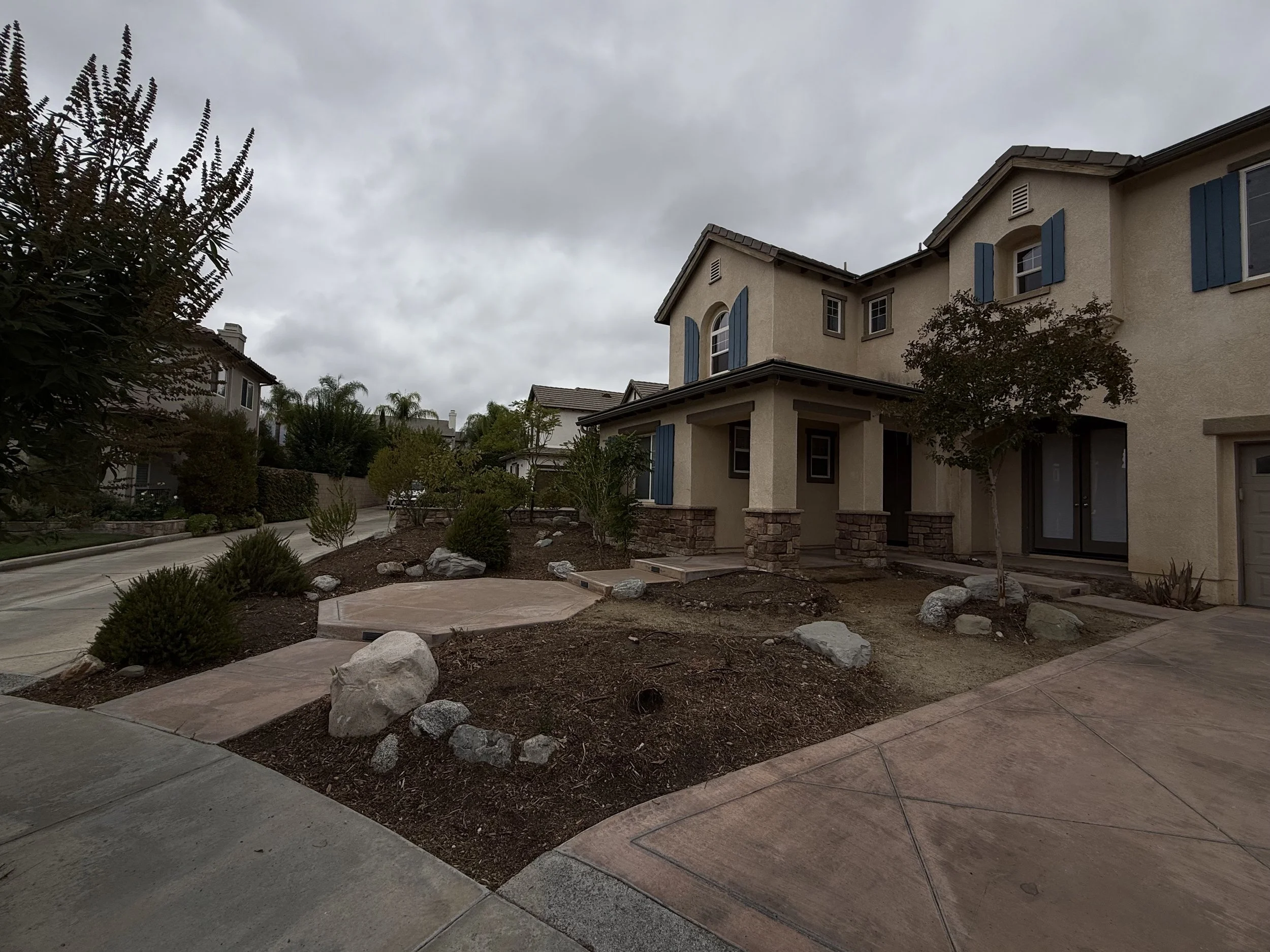 A residential neighborhood with two-story houses, a landscaped front yard, and a cloudy sky.