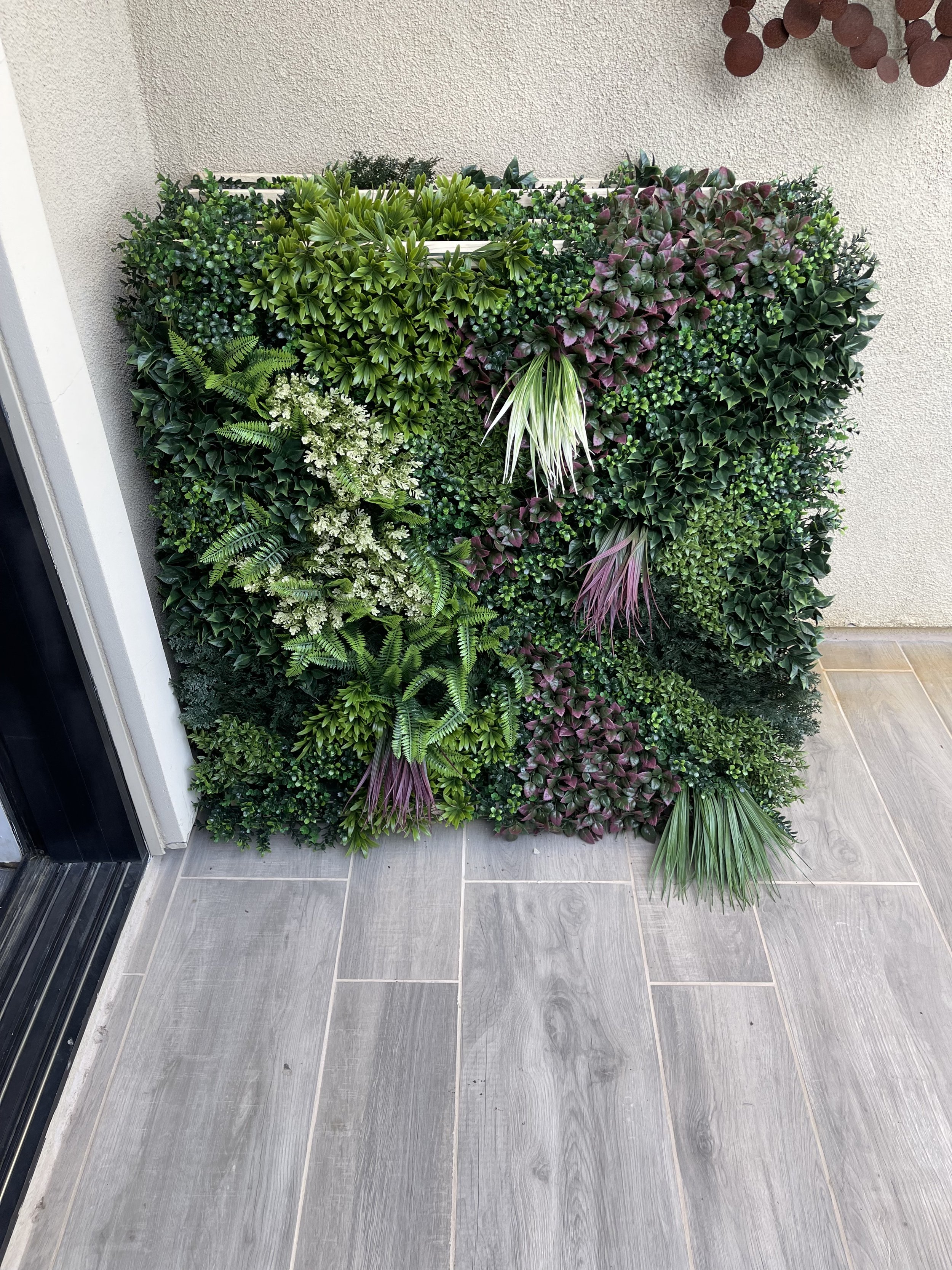 Decorative green wall with various types of plants next to a tiled floor and beige wall.