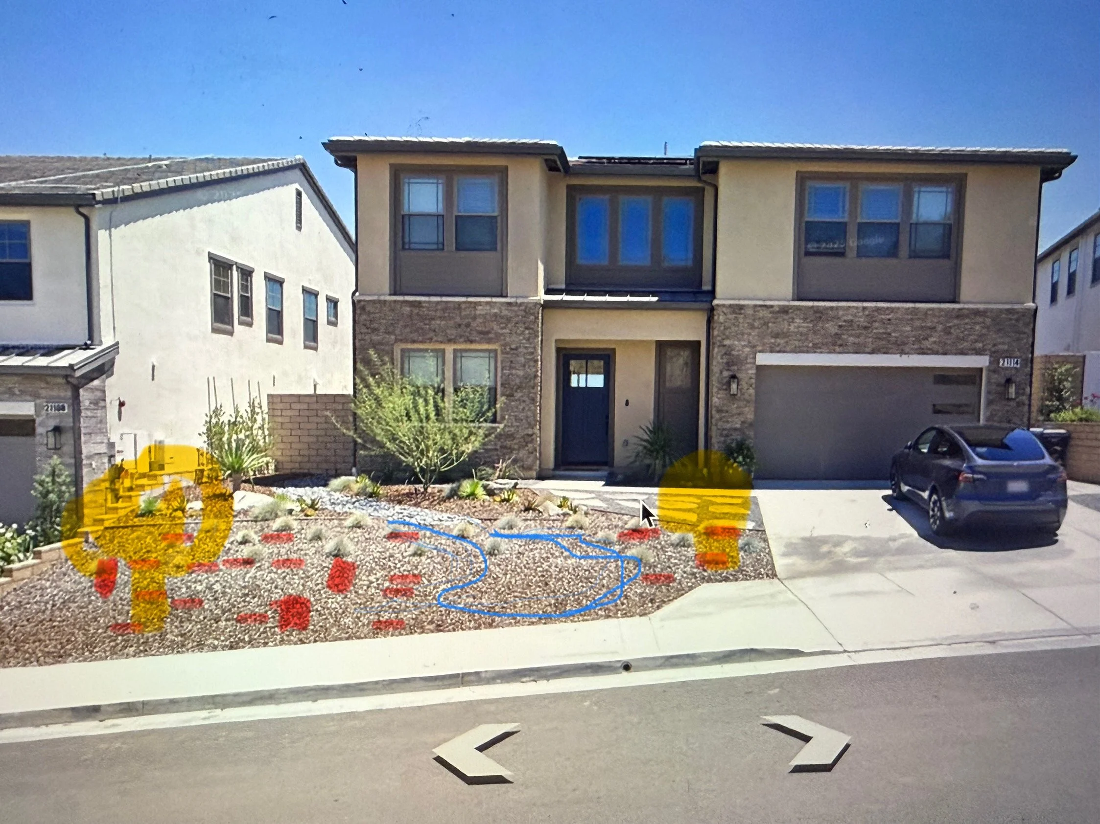Photo of a modern two-story house with beige and stone exterior, with a driveway, parked car, landscaping, and a clear blue sky.