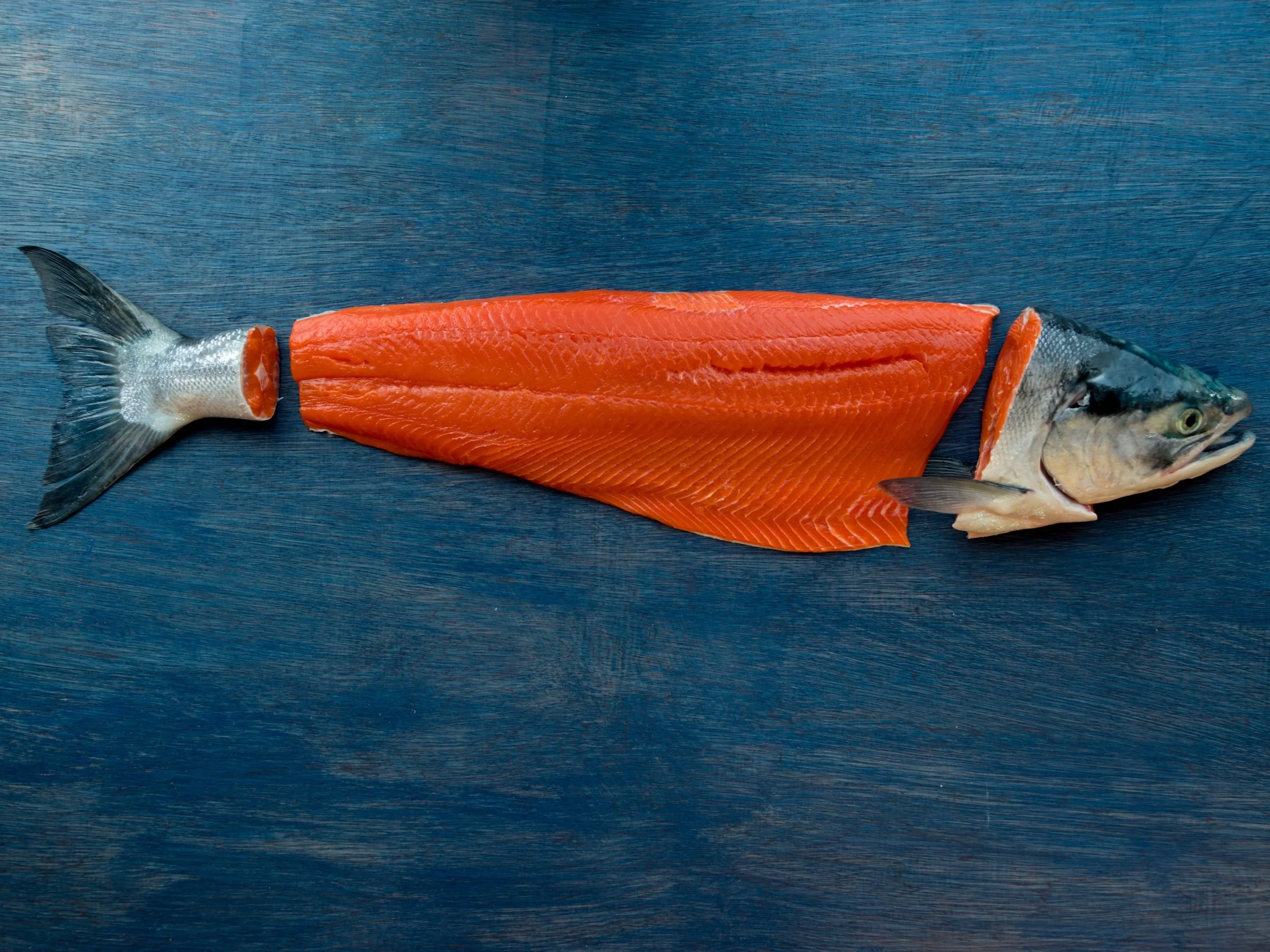 A fresh fish fillet and a whole fish on a dark wooden surface.