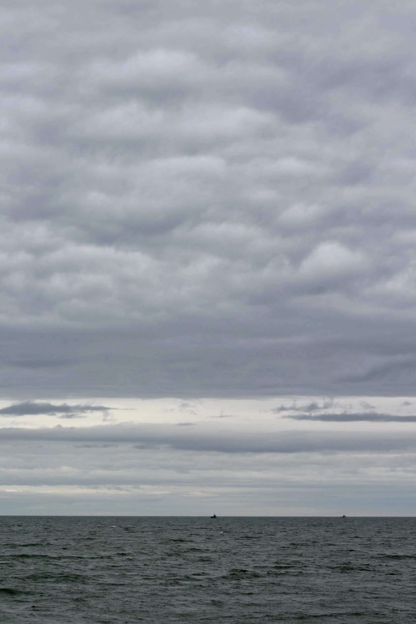 Overcast sky with thick, gray clouds above the ocean, small boats visible in the distance.