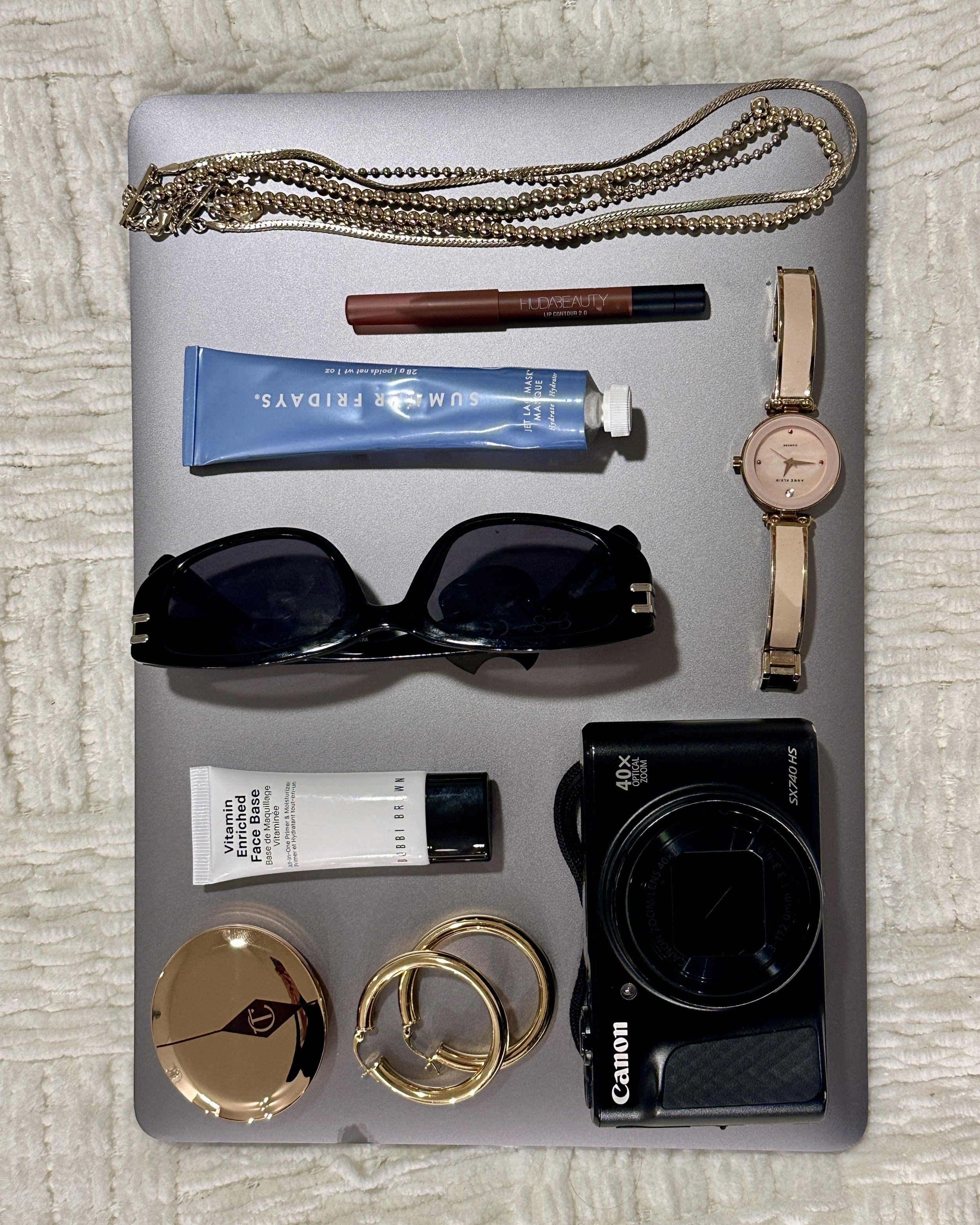 A collection of personal accessories and beauty products on a laptop, including jewelry, sunglasses, makeup, skincare, and a camera.