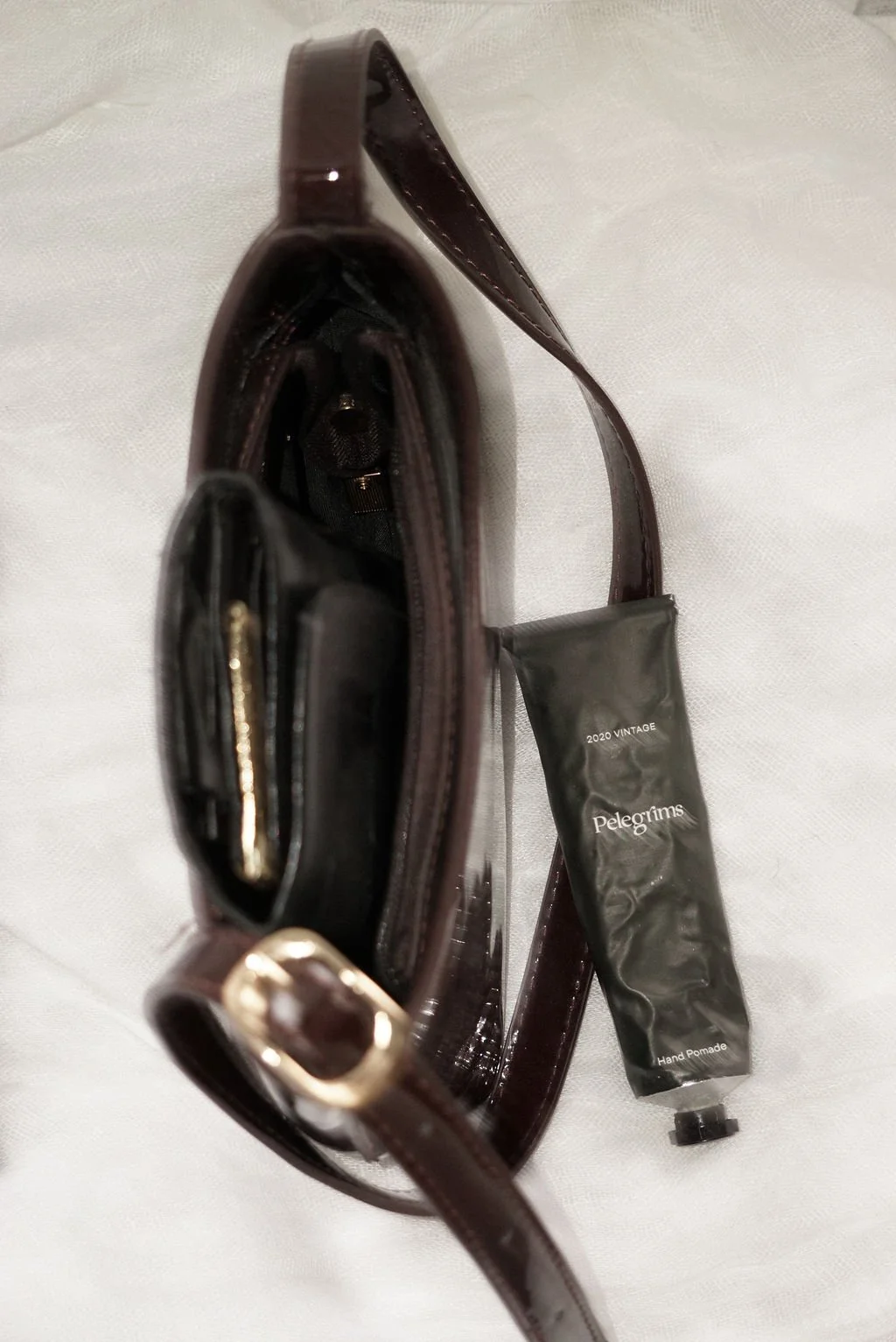 Open brown leather purse with a black tube of Pelégriims hand pomade inside on a white surface.
