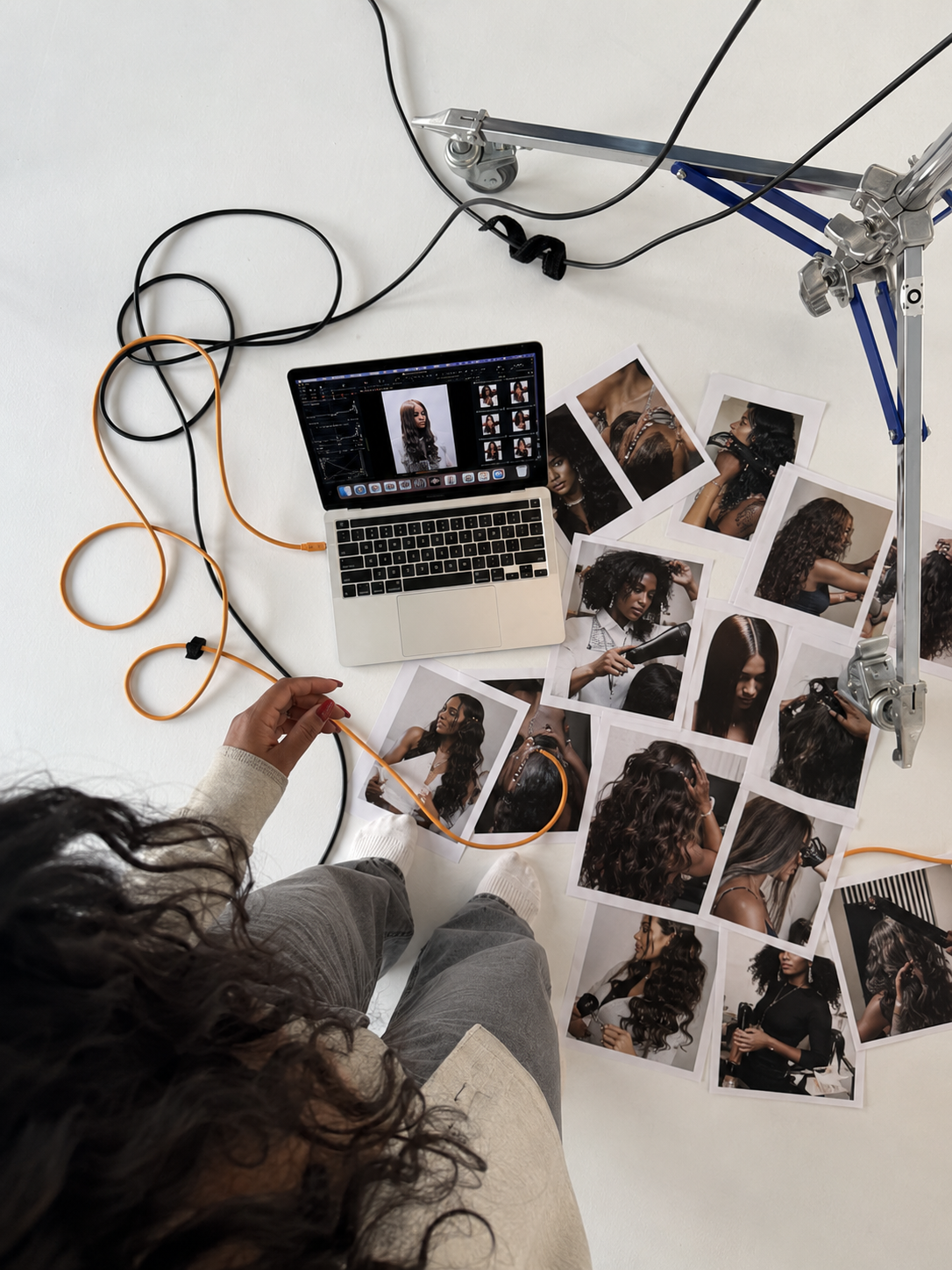 Photographer reviewing photos of women with curly hair and different hairstyles, scattered around a laptop on the floor, with art prints and photography equipment in the scene.