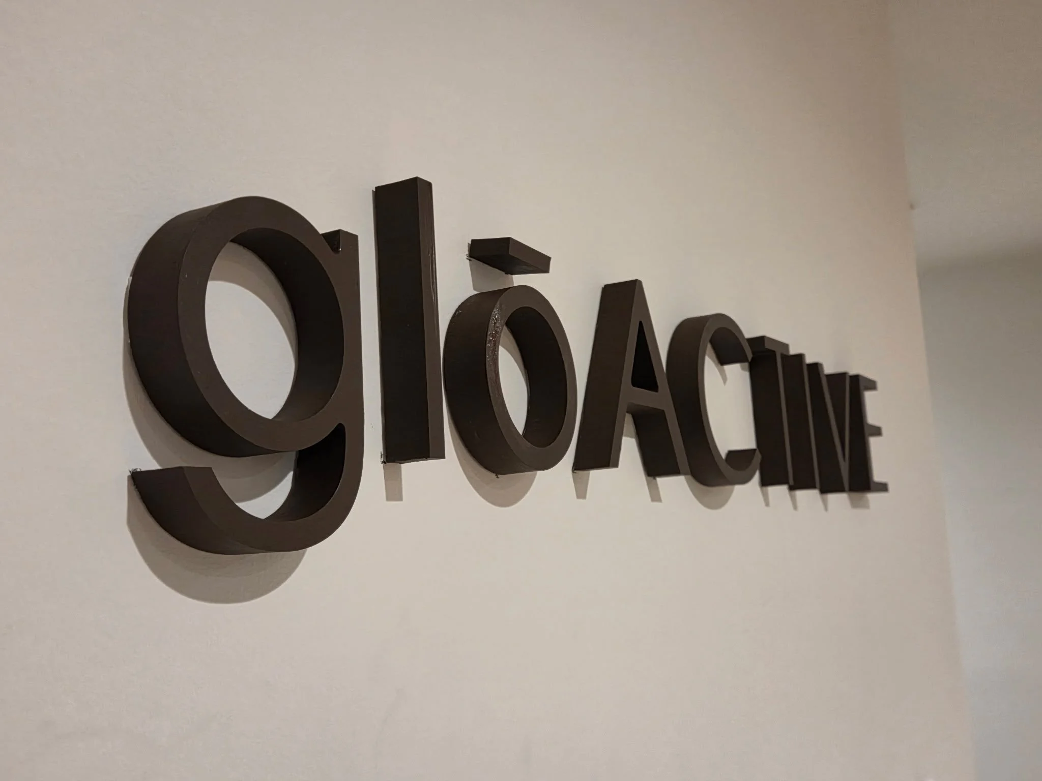 Close-up of black 3D letters spelling out 'glō ACTIVE' mounted on a white wall.