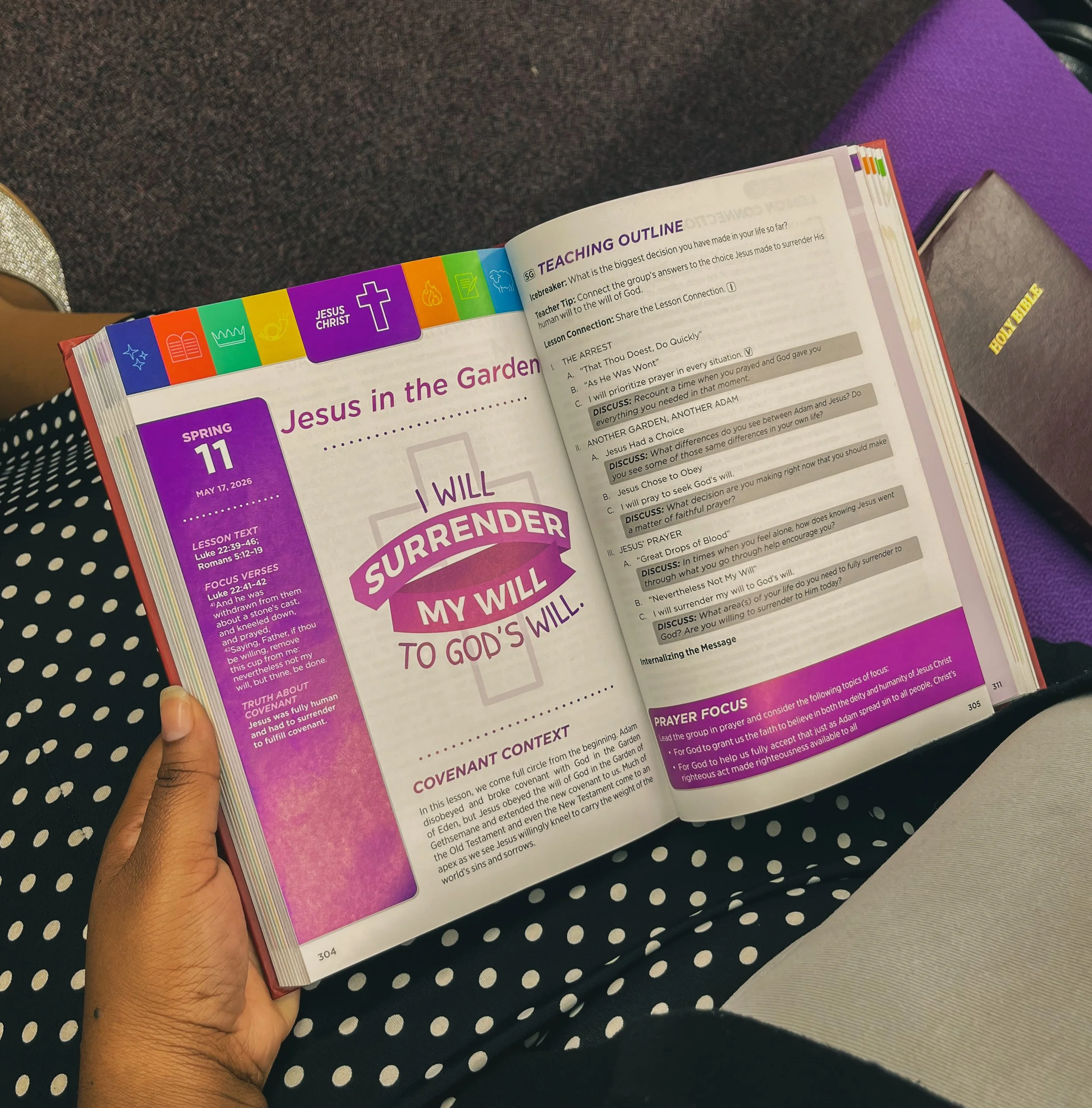 Open Bible with teaching outline and colorful tabs on the side, held by a person with medium skin tone against a polka dot fabric background.