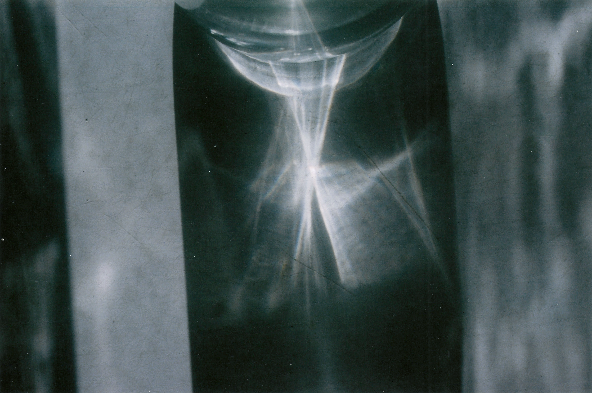A metallic, reflective surface with a shiny, curved, cup-like object in the center, reflecting light and creating bright highlights and reflections on the surrounding area.