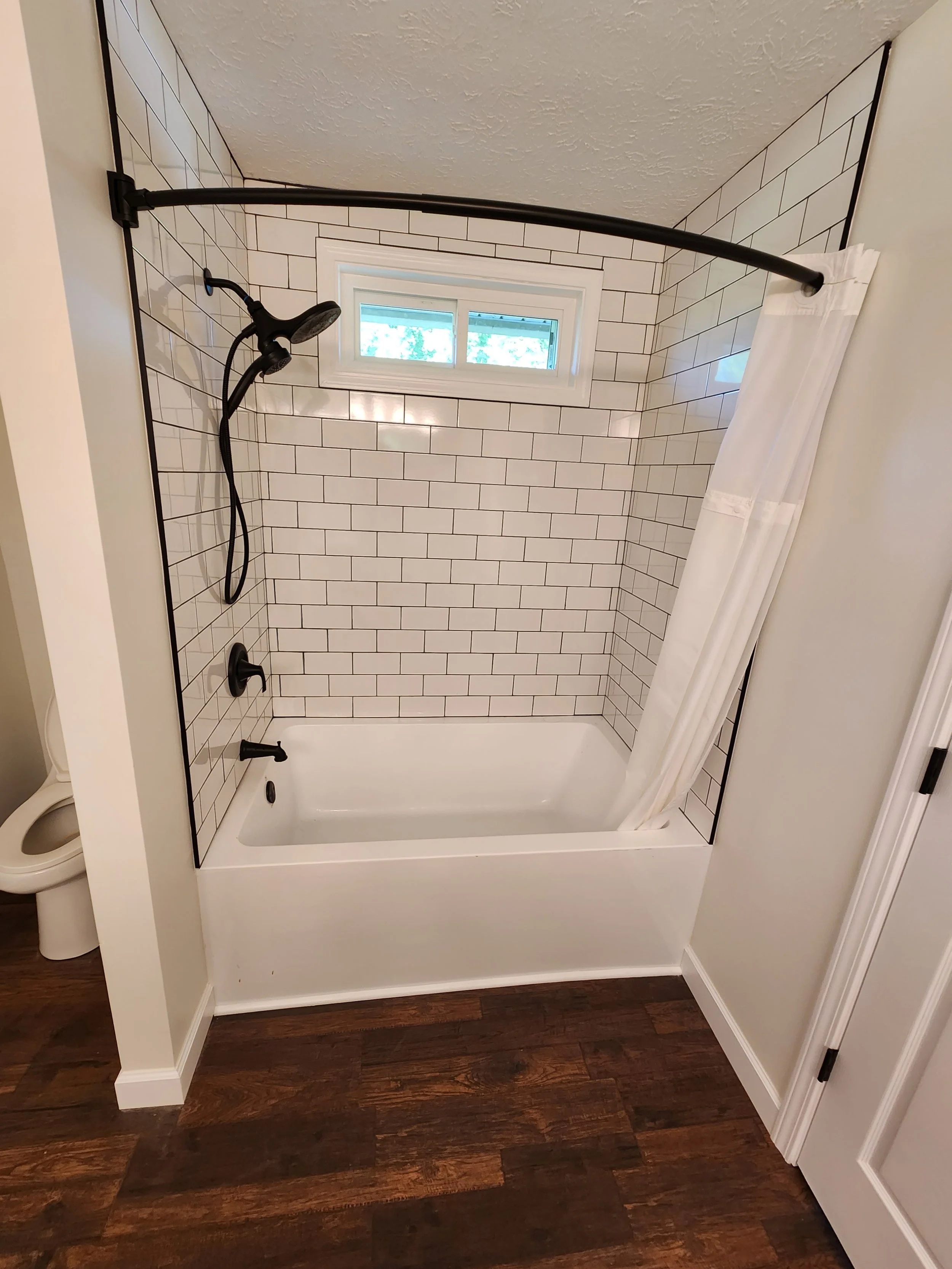 Bathroom shower with a white tub, white subway tiles, black shower hardware, a small window, and a white shower curtain on a curved shower rod.