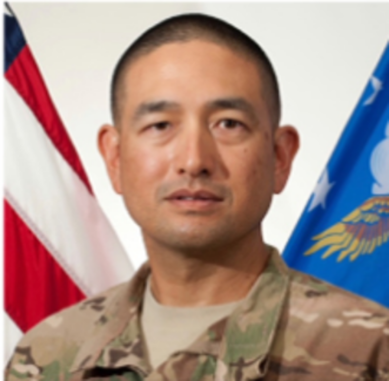 Michael Morabe in Airforce active-duty uniform with the American and military flags in the background.