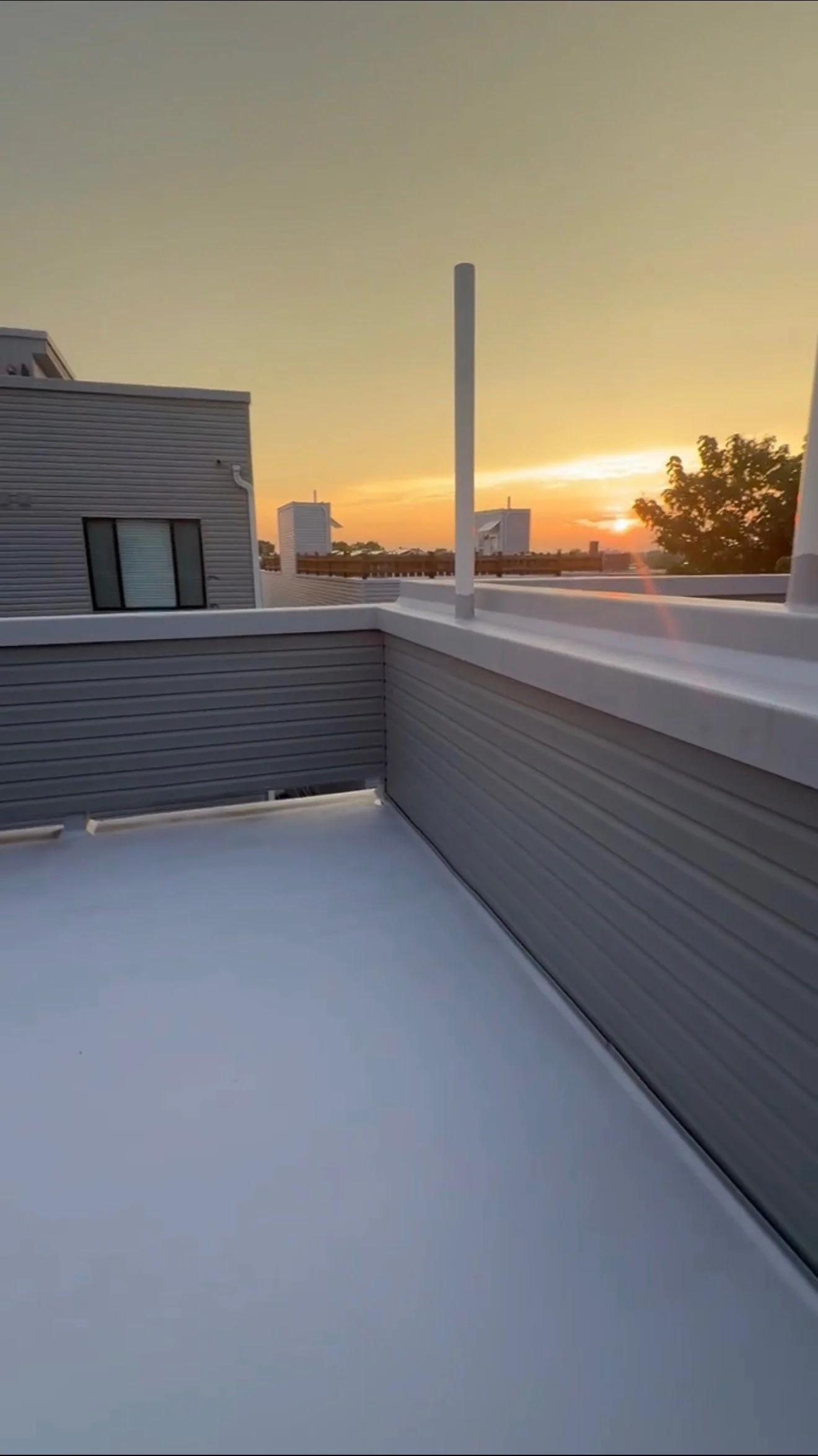 Balcony with gray siding walls and a view of neighboring buildings at sunset.