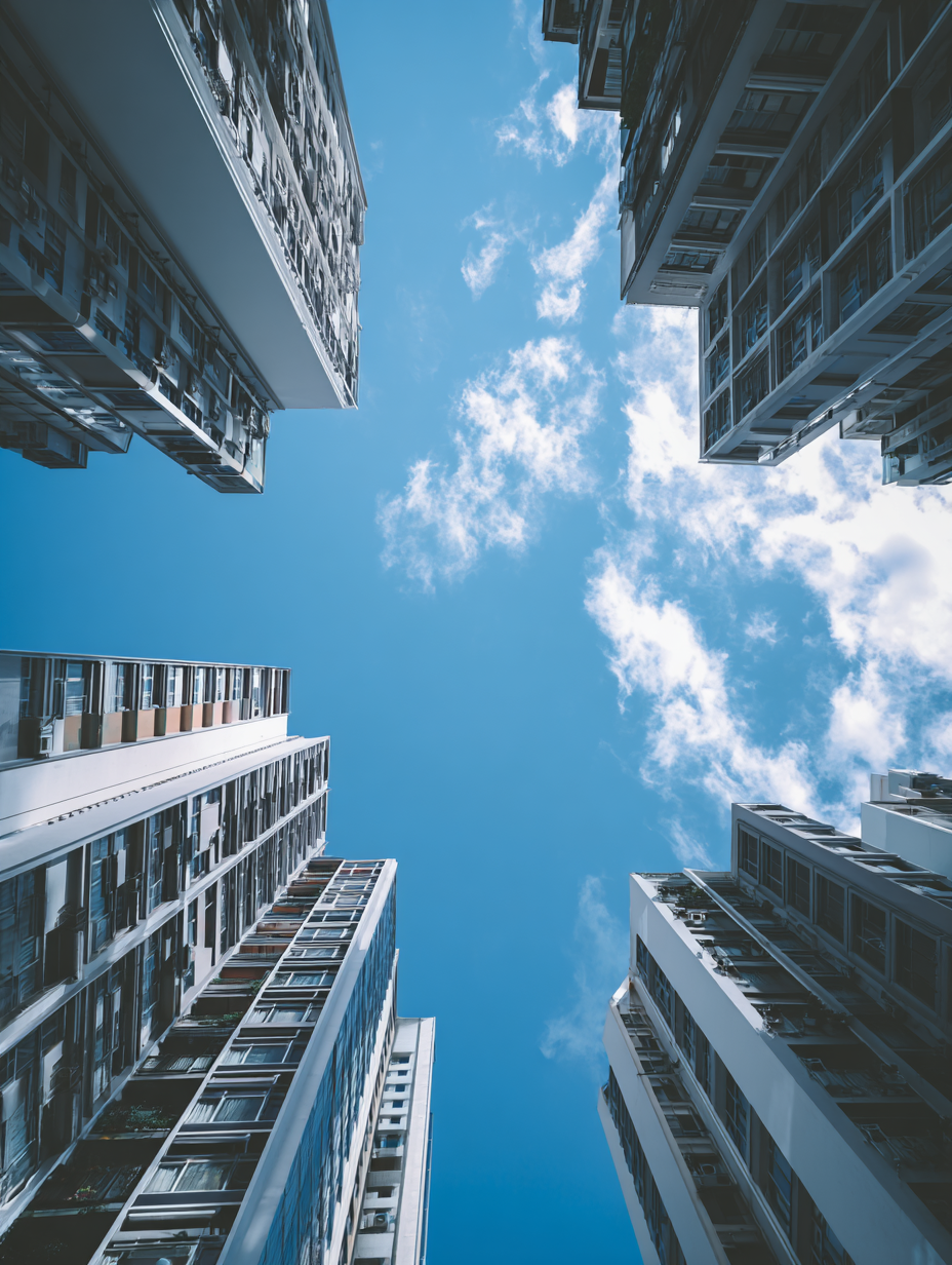 Looking up at tall apartment buildings with balconies and windows, framing a bright blue sky with some white clouds.