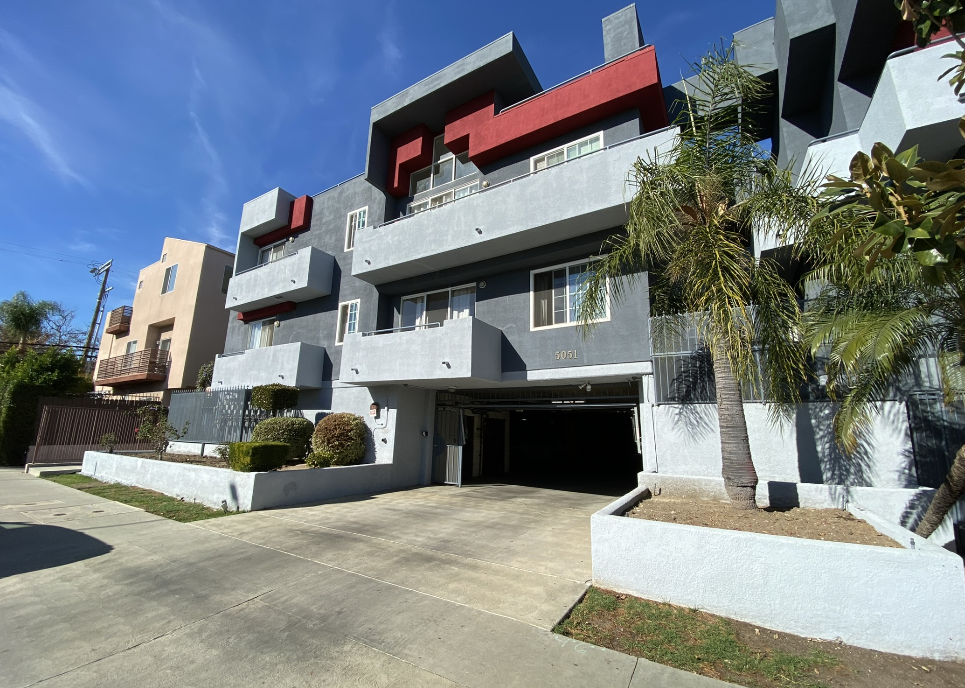Modern apartment building with balconies and palm trees, clear blue sky.