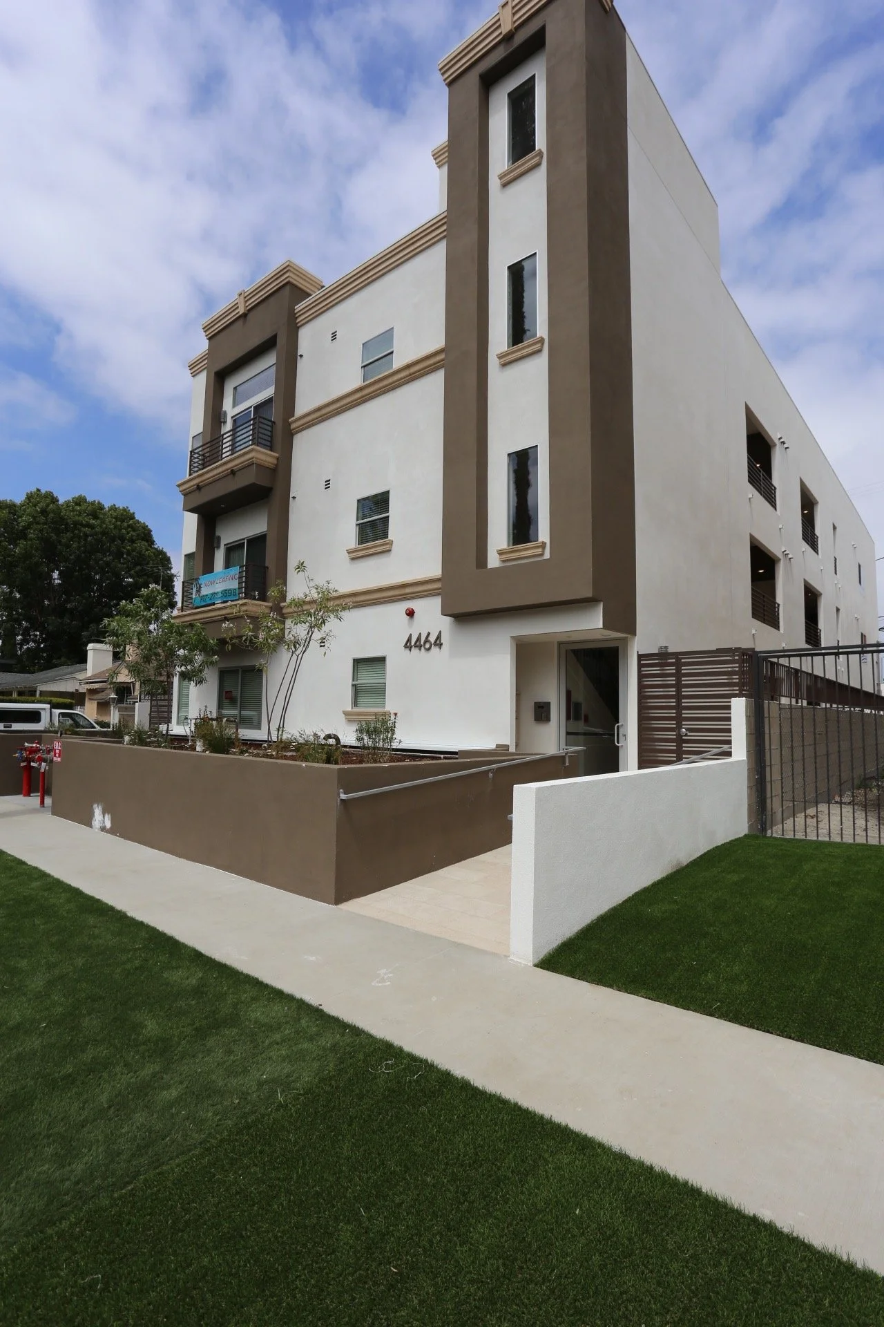 Modern three-story apartment building with beige and white exterior, balconies, and neatly landscaped lawn.
