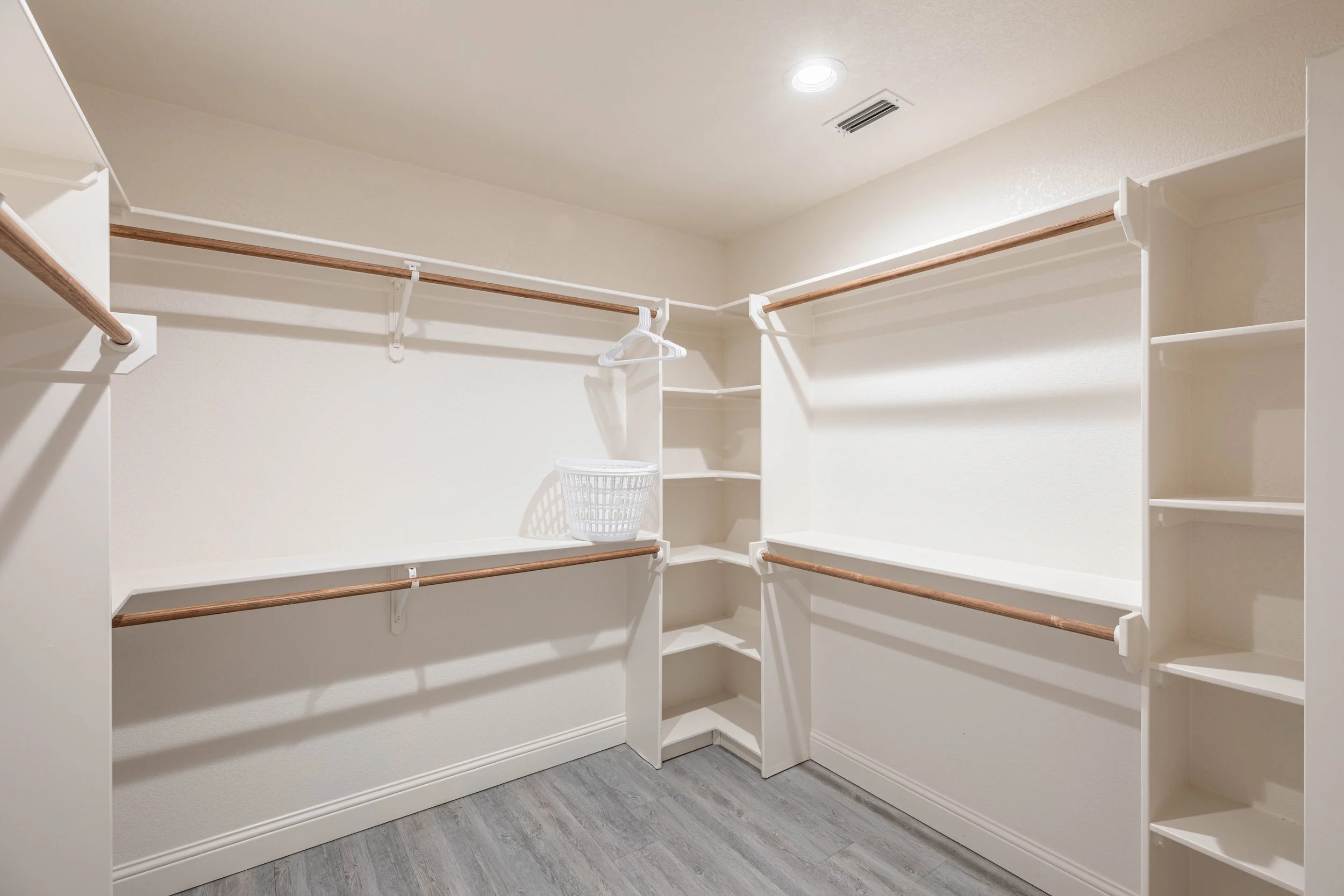 Empty white walk-in closet with built-in shelves and hanging rods