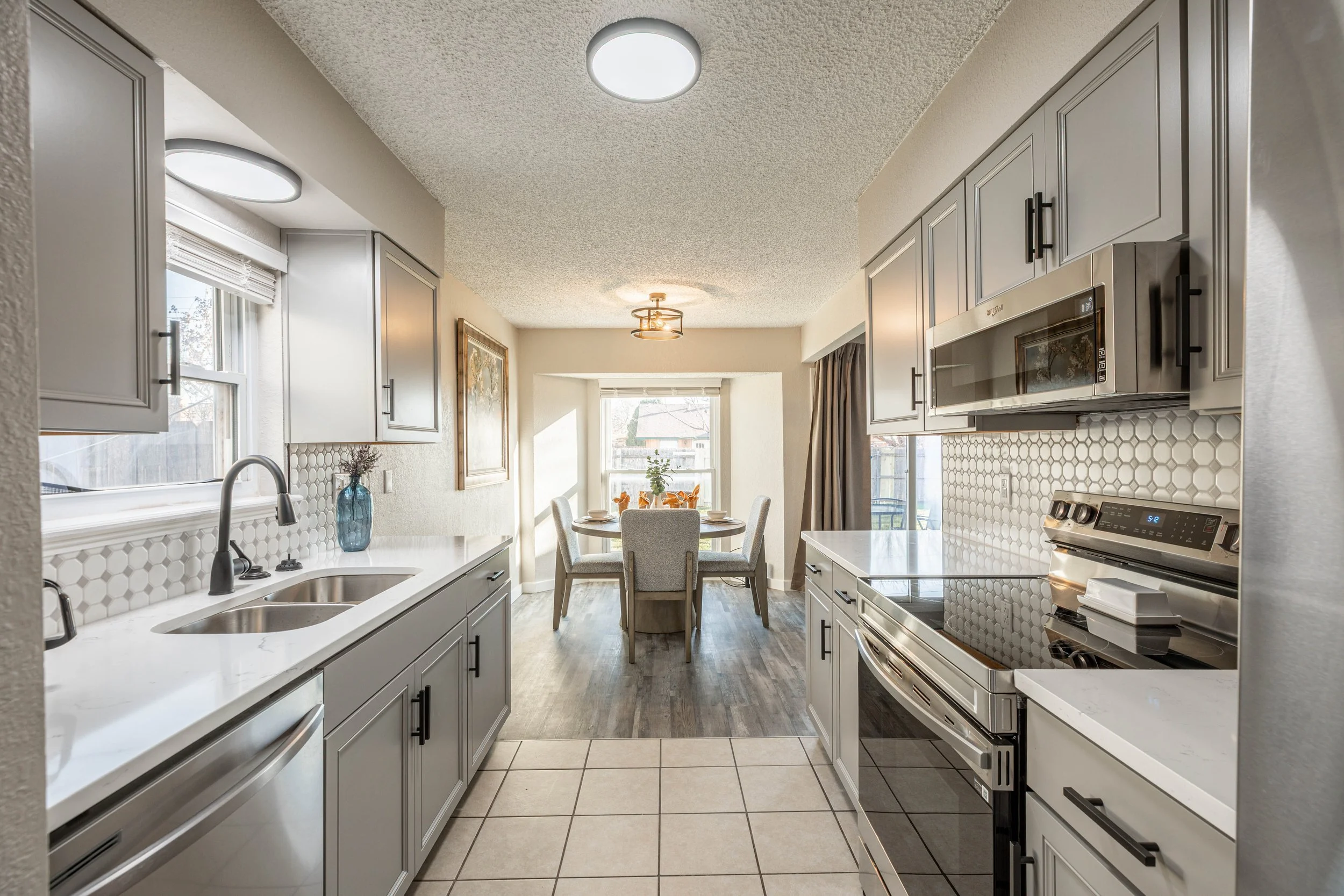 Bright kitchen with white cabinets, stainless steel appliances, and a dining area with a table and chairs near large windows.