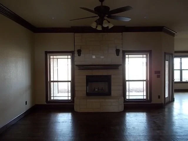 Empty living room with fireplace, two windows, ceiling fan, and hardwood floors.