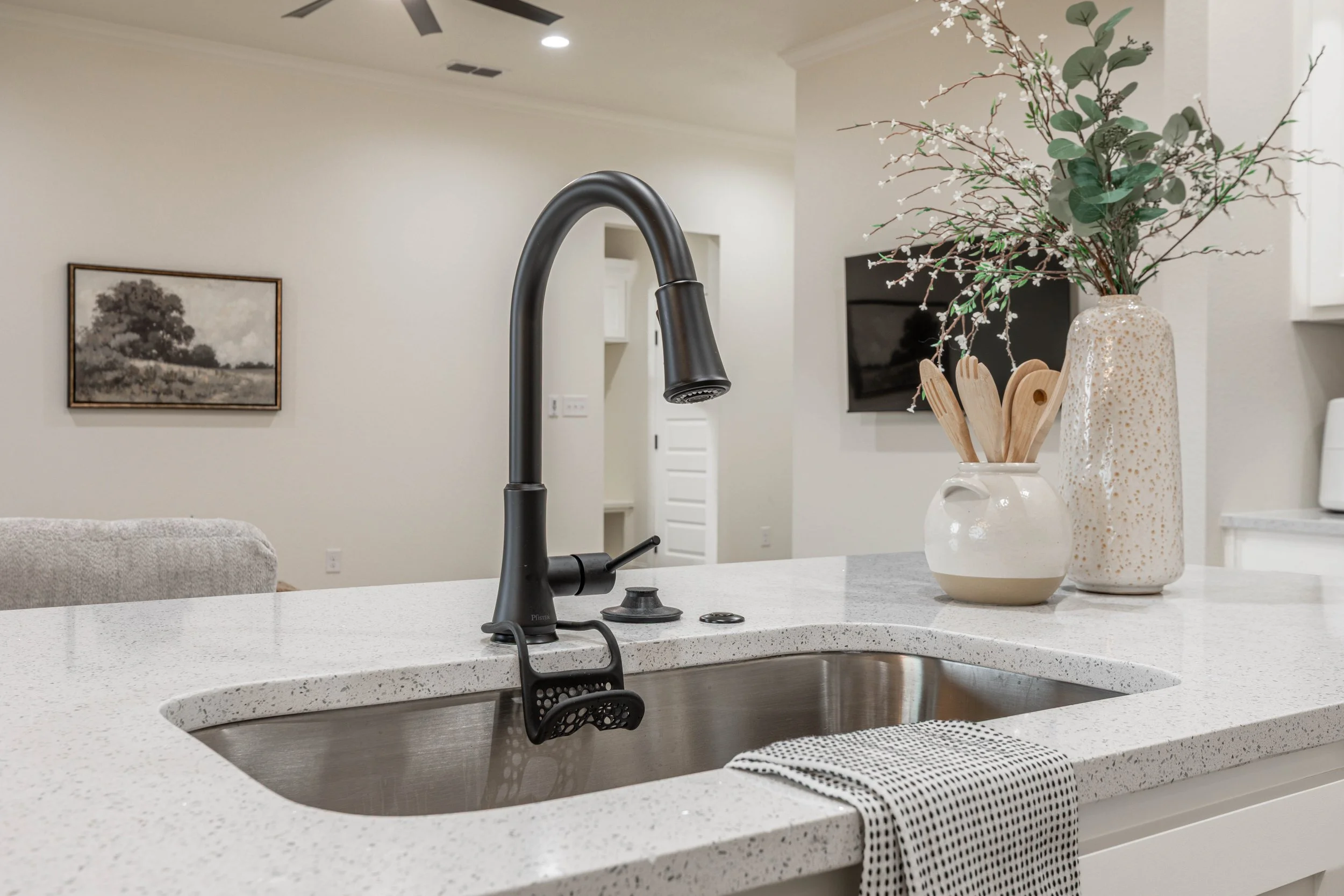 A kitchen countertop with a black faucet, a white speckled countertop, and decorative vases with green foliage.