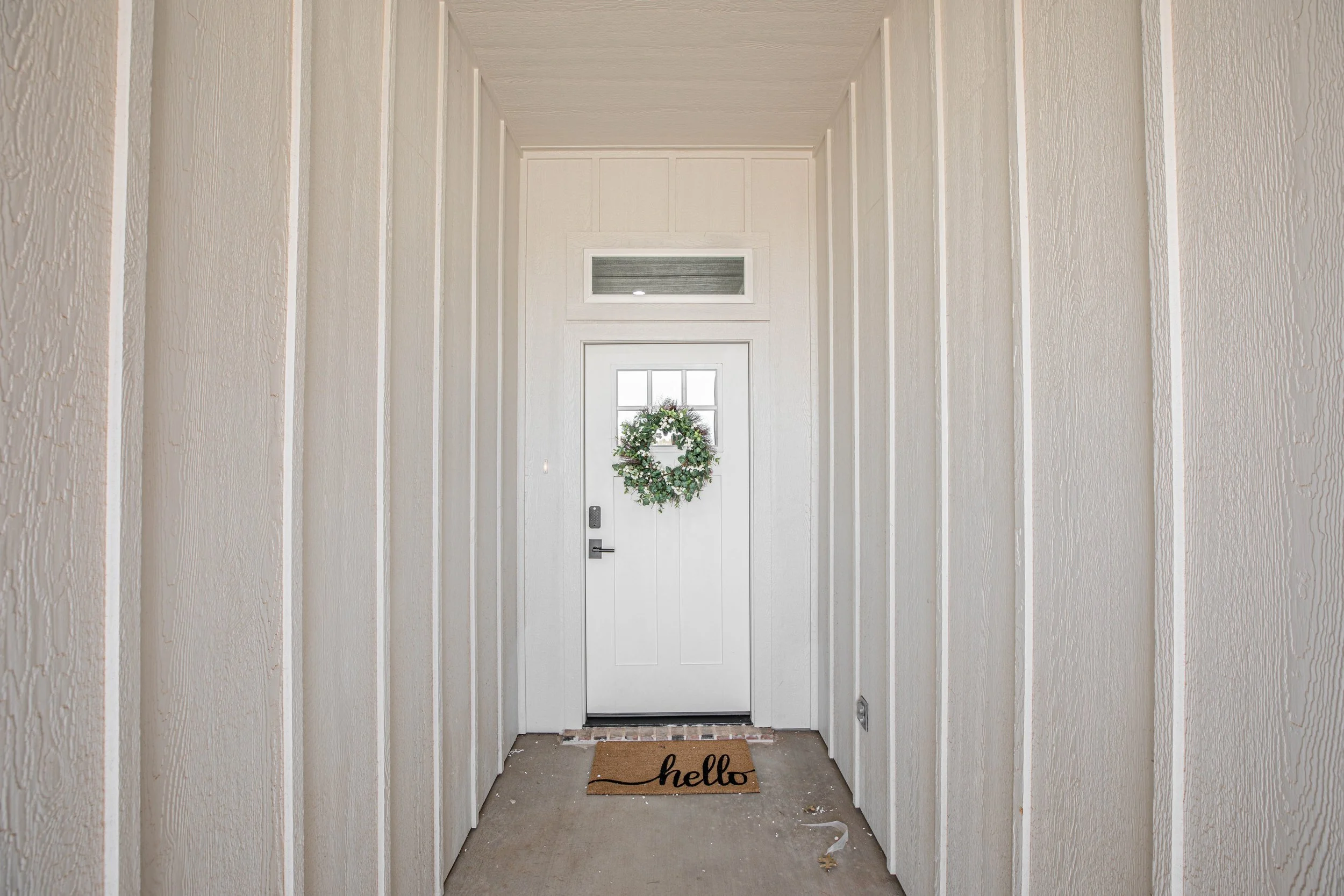 Front door with a wreath and a doormat that says 'hello' in an entryway with white paneled walls.