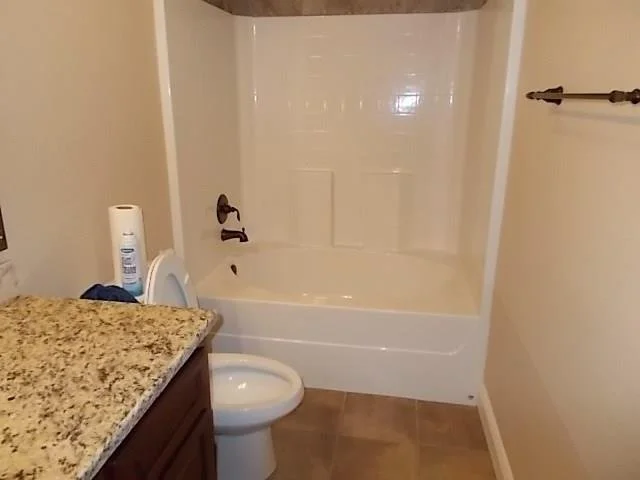 Bathroom with a bathtub/shower combo, a toilet, a countertop with a granite surface, and a wall-mounted towel rack.