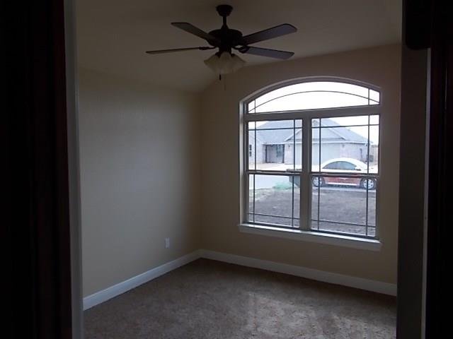 Empty room with beige walls, a large arched window, ceiling fan, and carpeted floor.