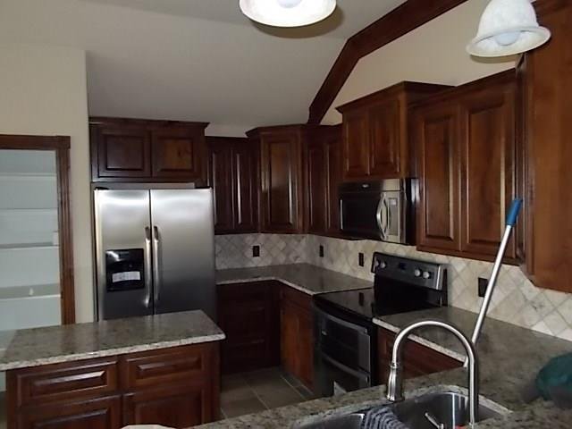 Kitchen with wooden cabinets, stainless steel refrigerator, microwave, stove, and a countertop with a sink. A mop is leaning against the countertop.