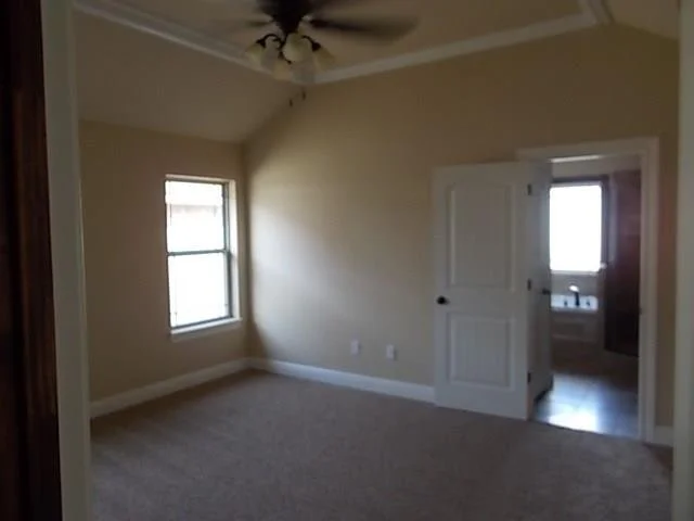 Empty bedroom with beige walls, a window, a ceiling fan, and an open door leading to a bathroom.